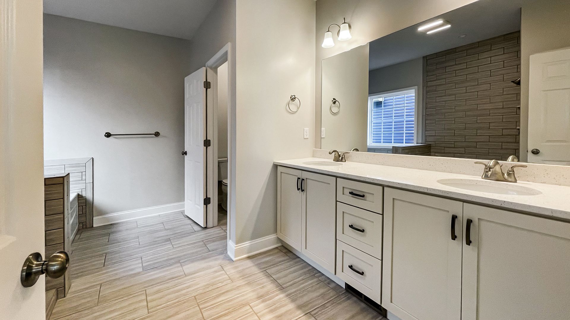 Owner's Bath with white cabinetry, double vanity with large mirror above, ceramic tile floor, tub, and enclosed water closet