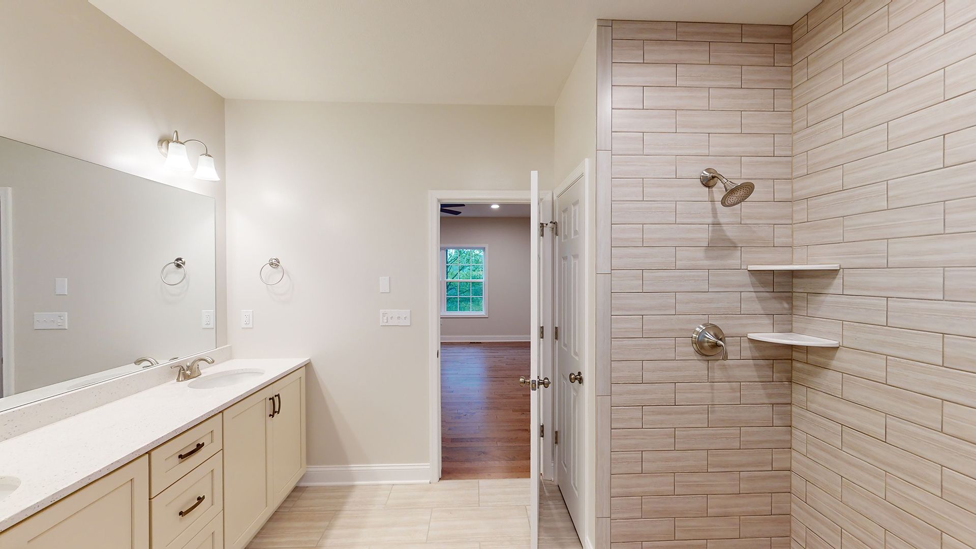 Owner's Bath - double vanity with large mirror above, shower with ceramic tile surround and corner shelves - facing doorway into bedroom.