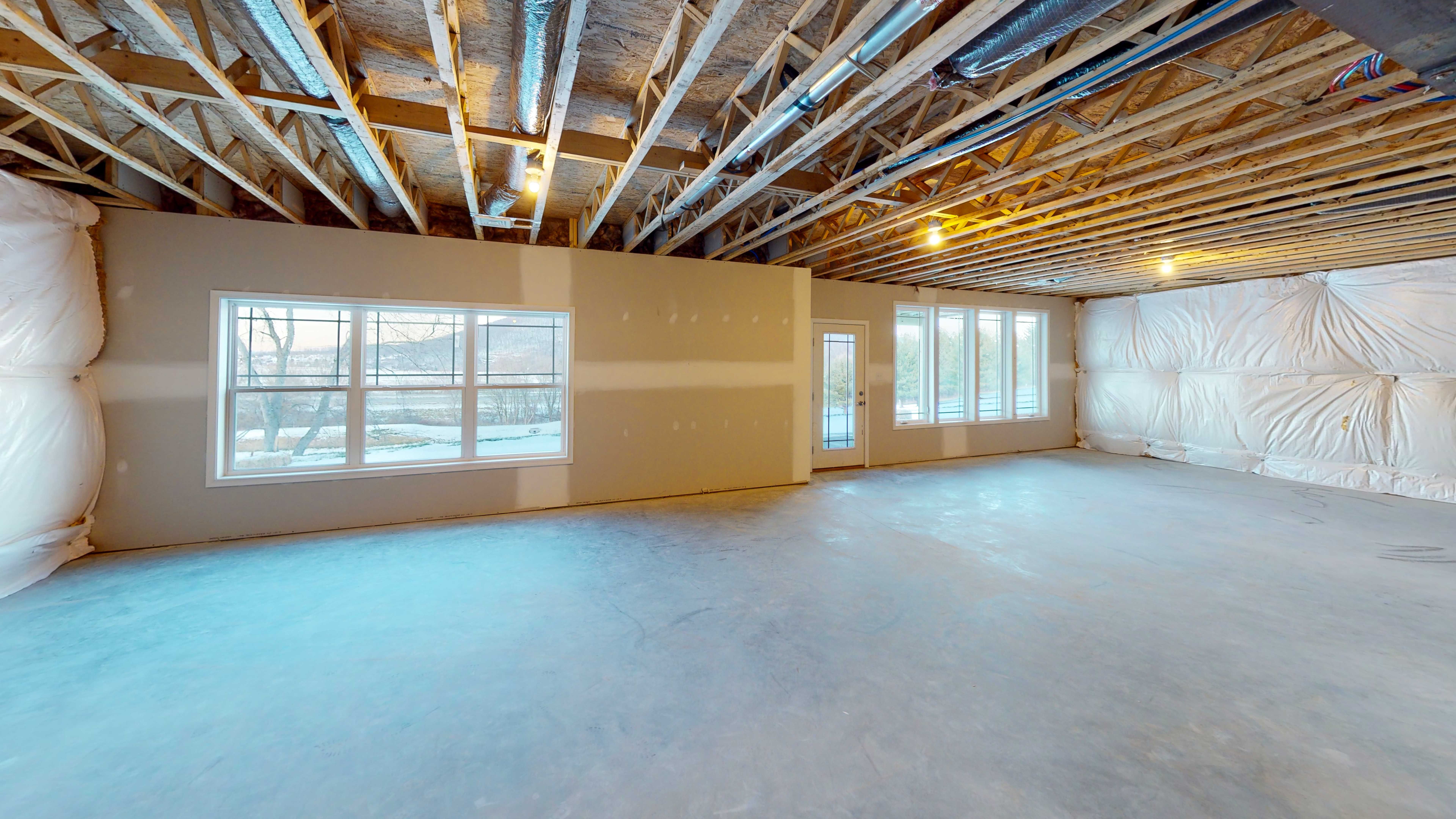 Unfinished basement with wall of windows and doorway to outside.