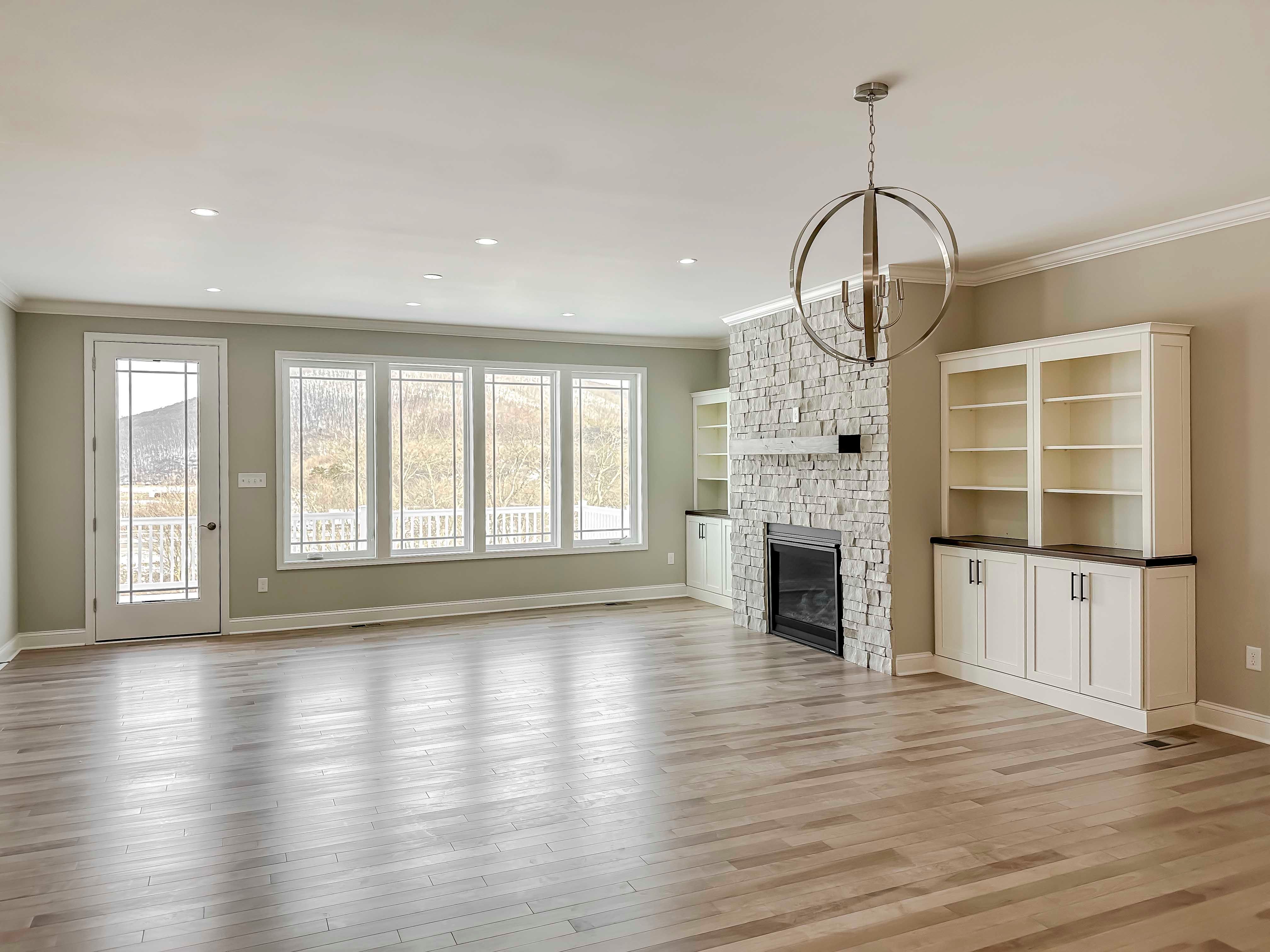 Family room with hardwood flooring, stone fireplace flanked by cabinets, and rear wall of windows