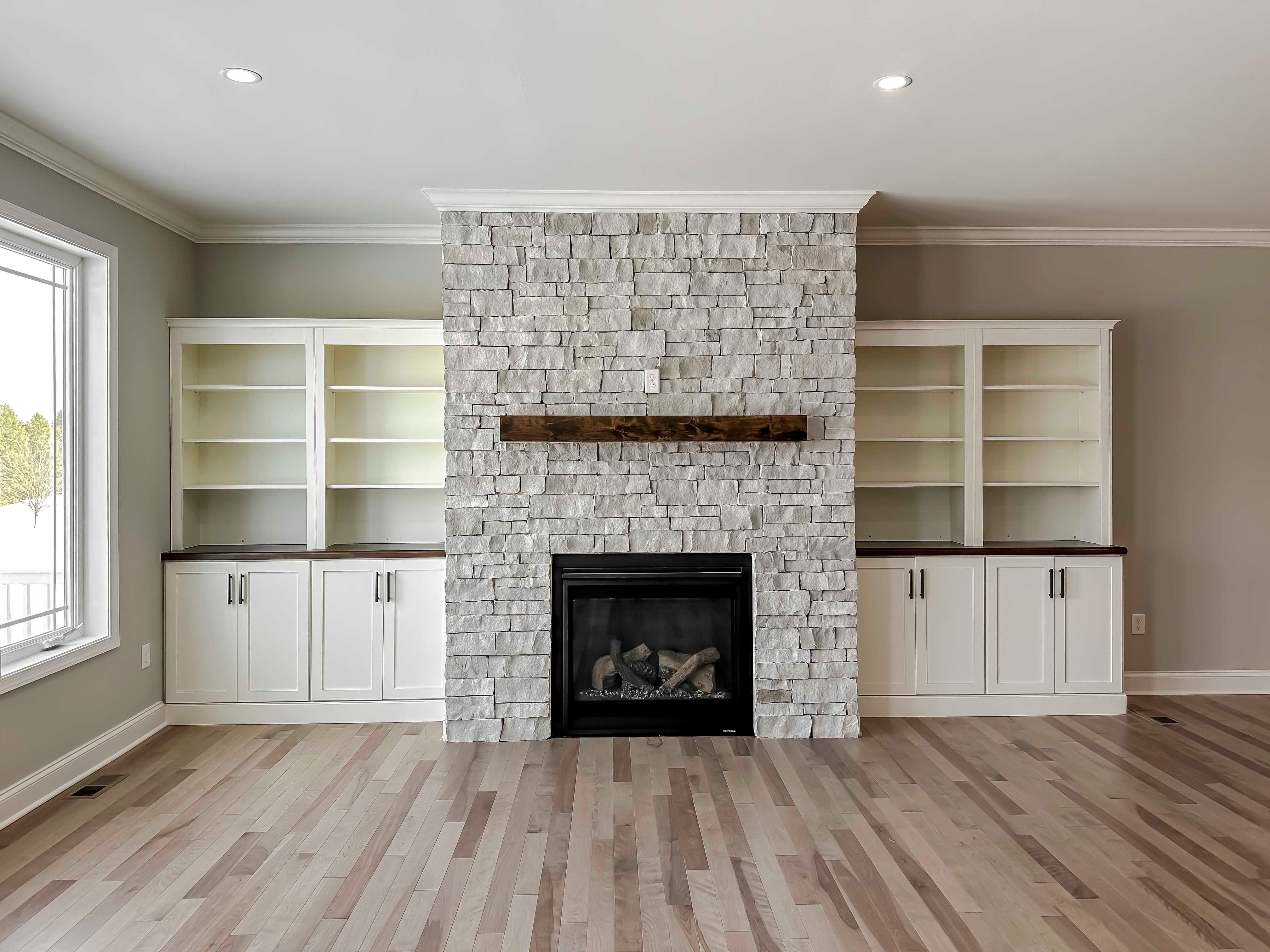 Stone fireplace flanked by cabinets, and rear wall of windows