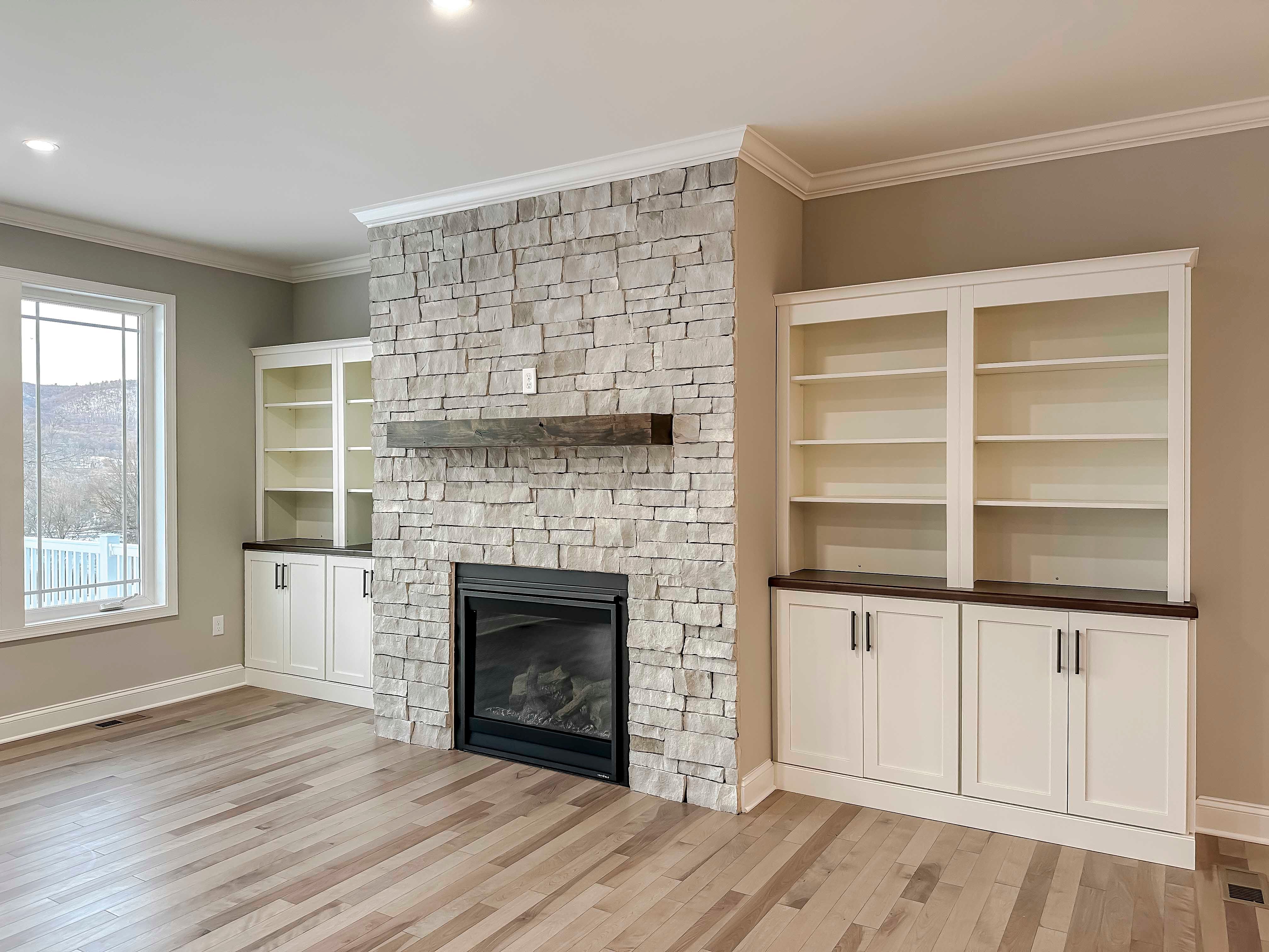 Stone fireplace flanked by cabinets, and rear wall of windows