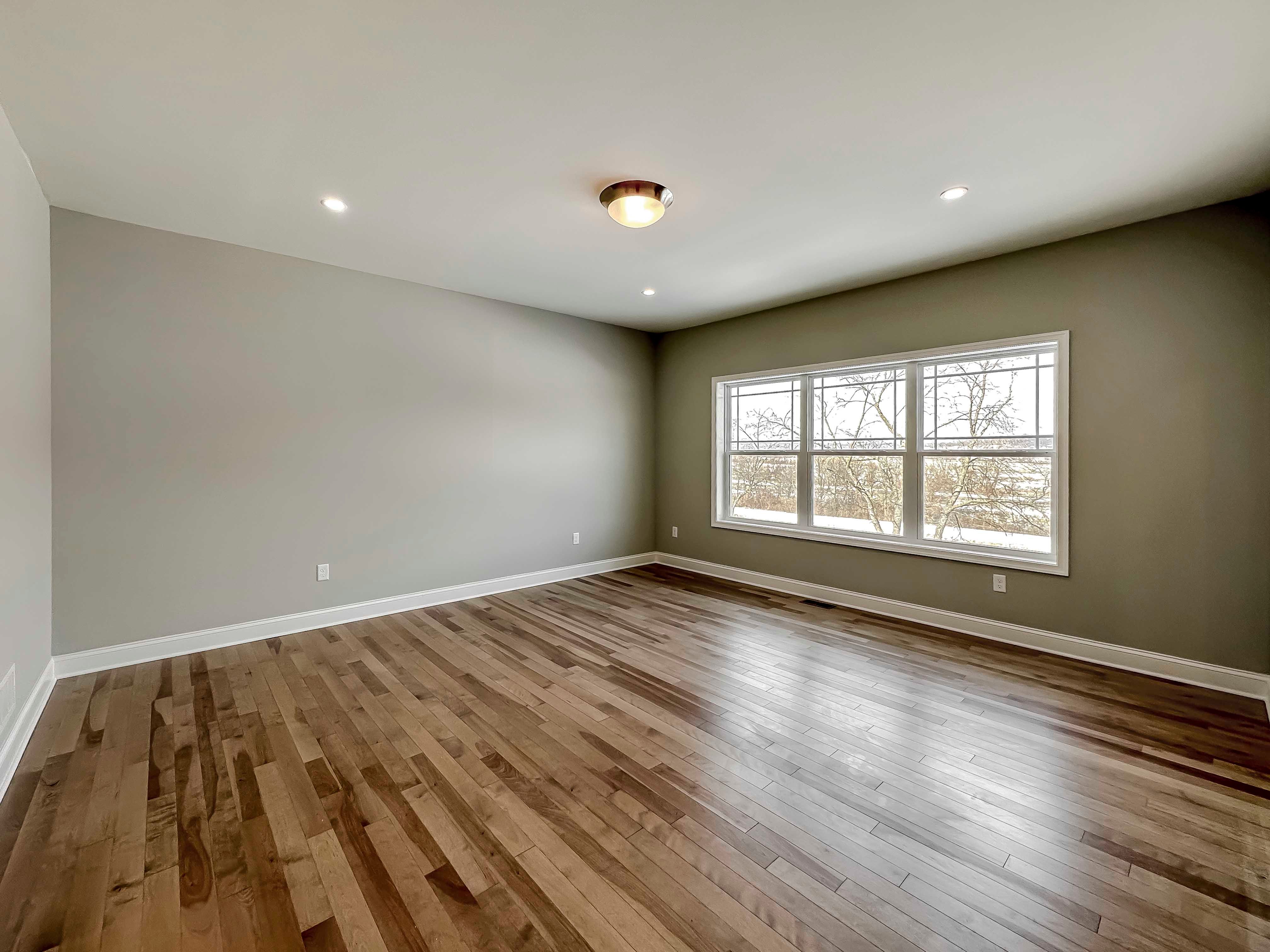 Bedroom with hardwood flooring and triple windows on rear wall