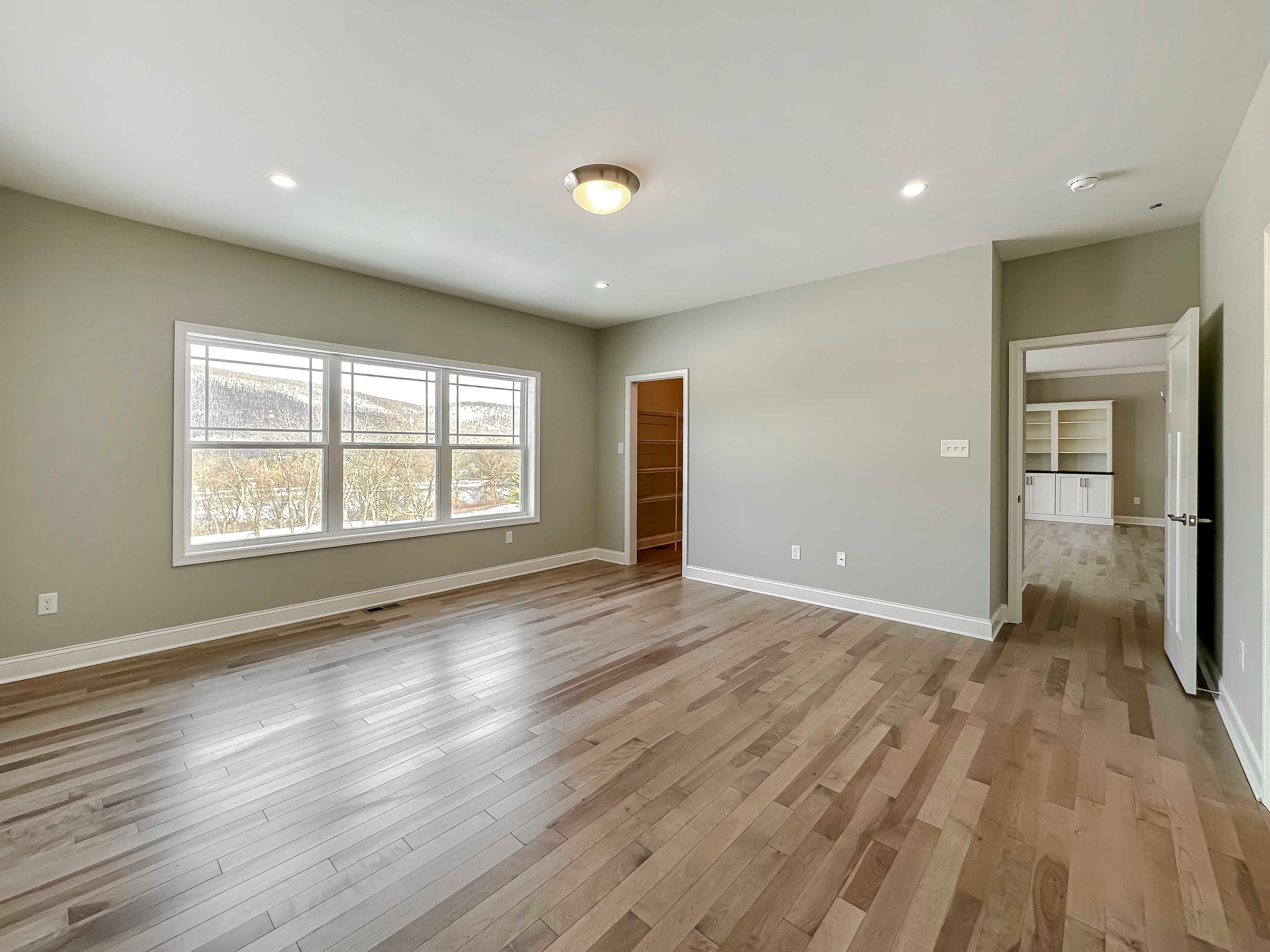 Bedroom with hardwood flooring and triple windows on rear wall