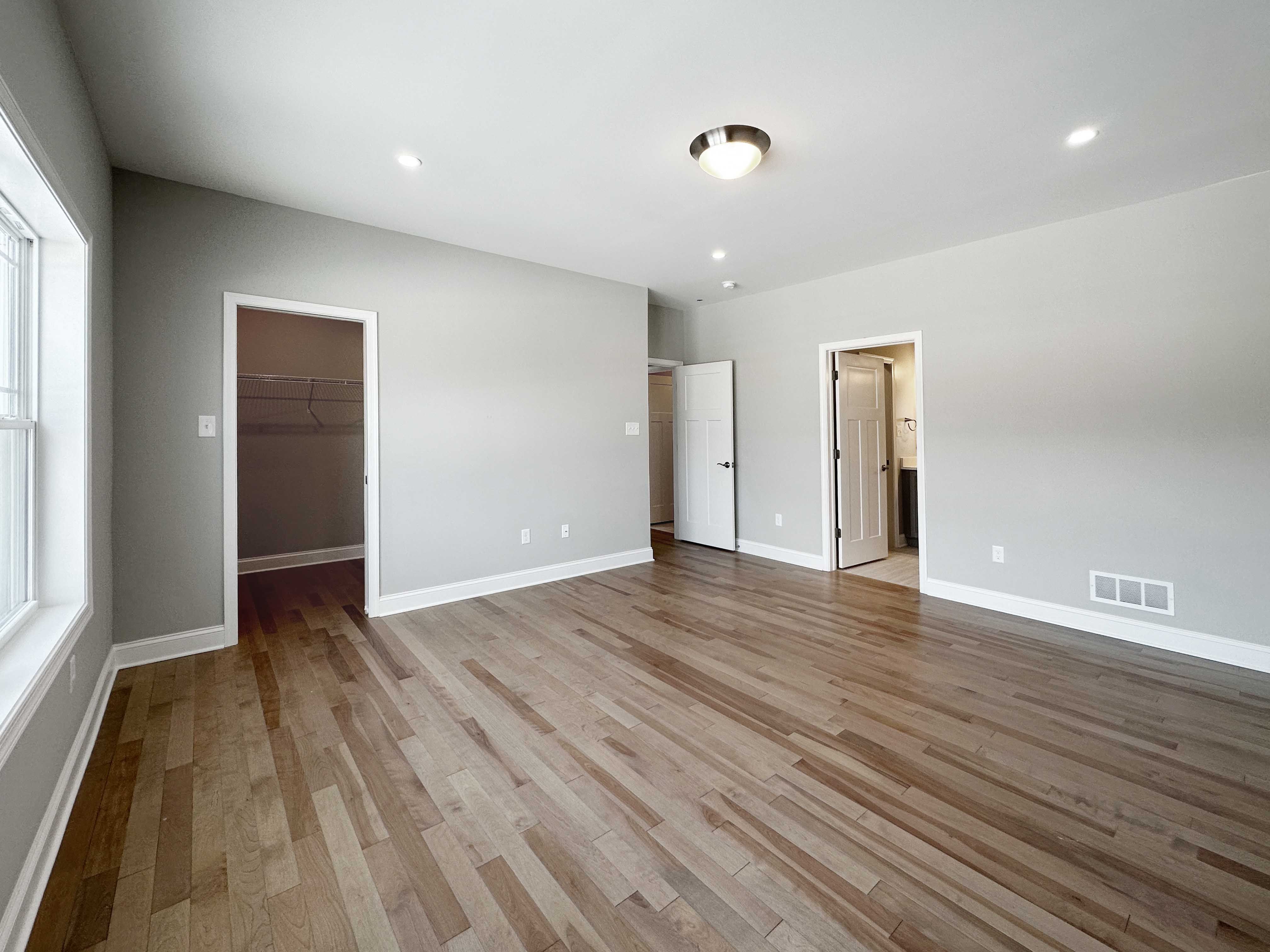 Bedroom with hardwood flooring - facing doorways to bathroom, closet and hall