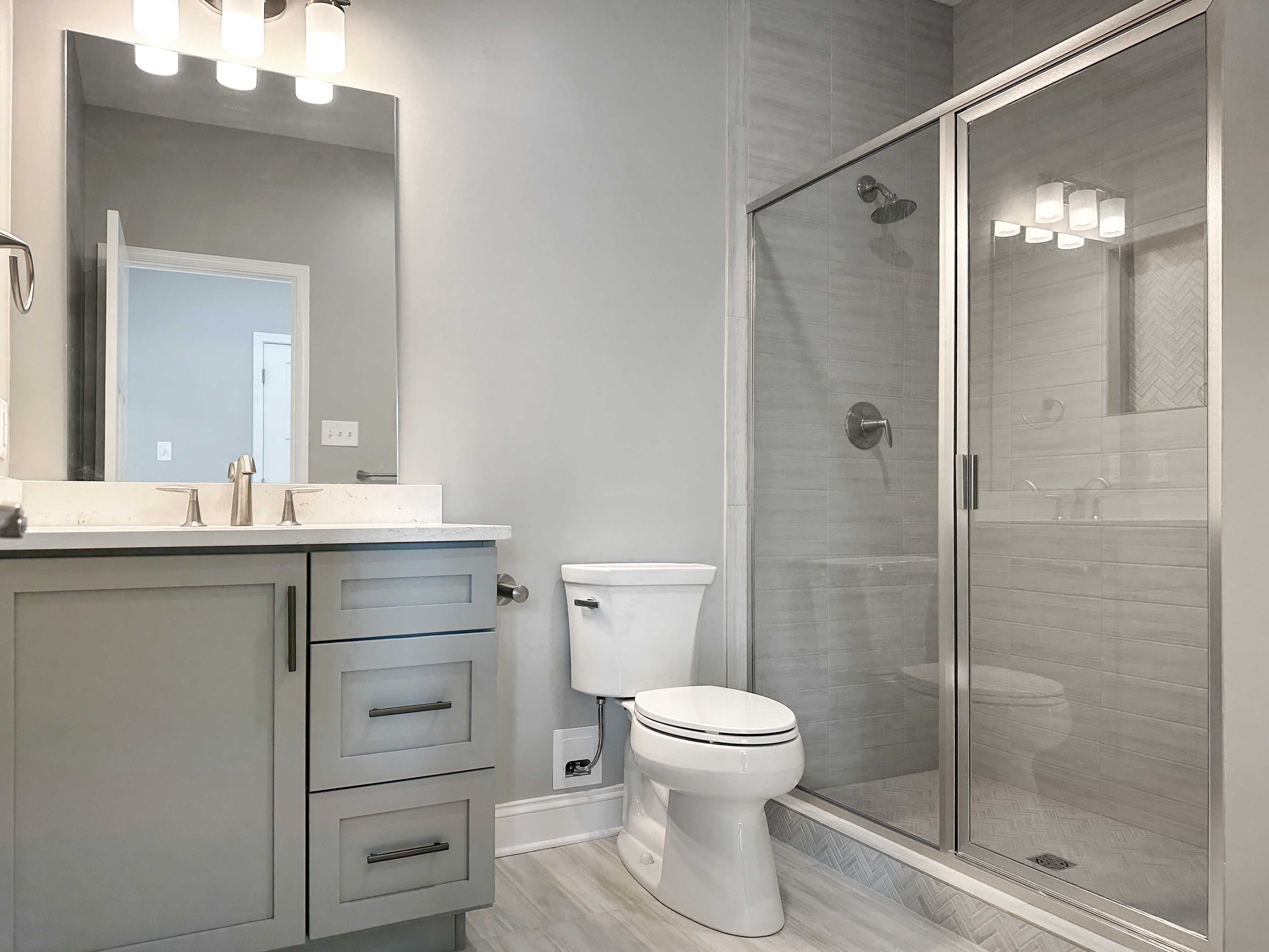 Bathroom with single vanity with gray cabinets, toilet and shower with ceramic tile surround.