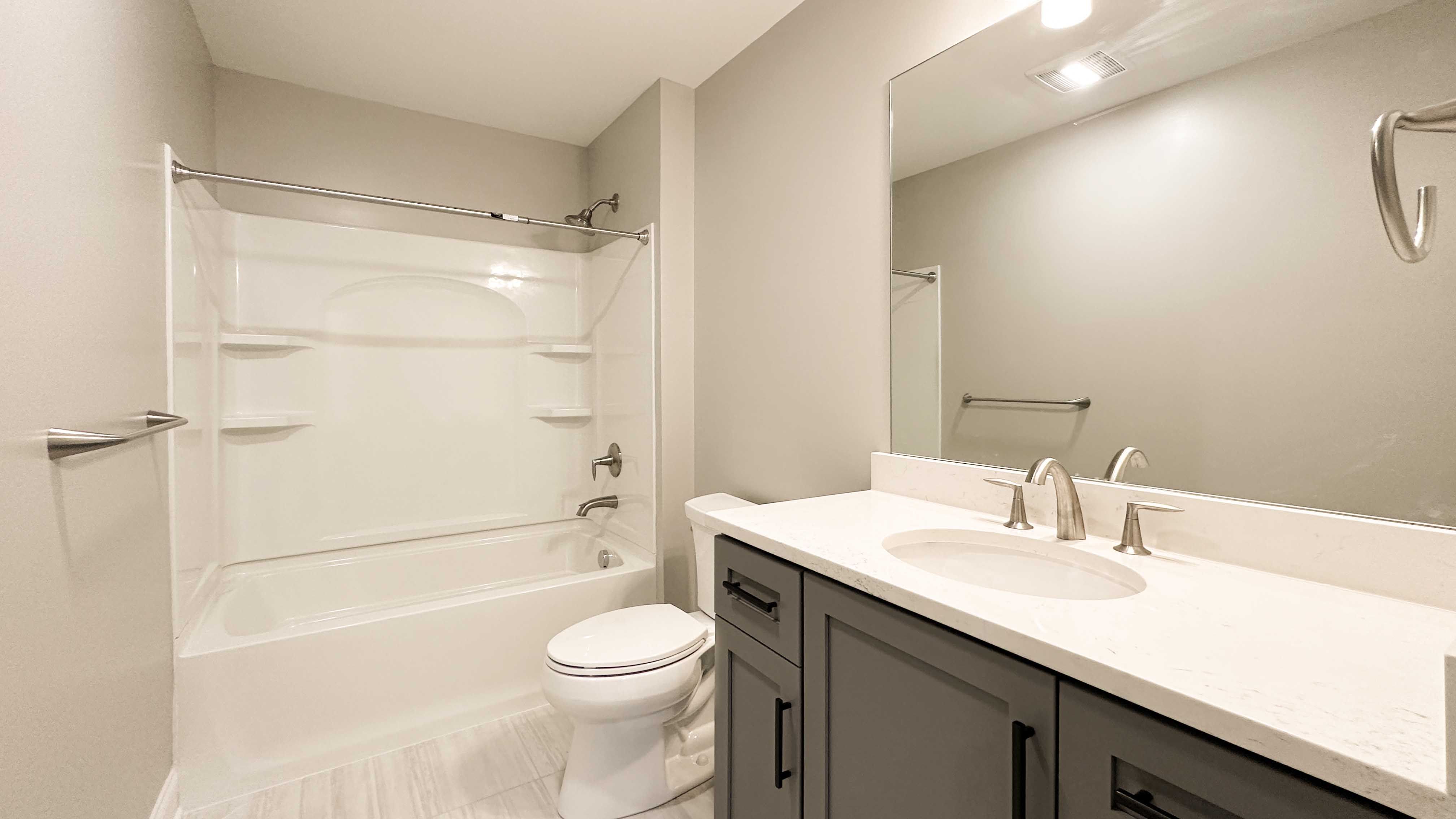 Bathroom with single vanity, large mirror, toilet and tub shower combination with corner shelves