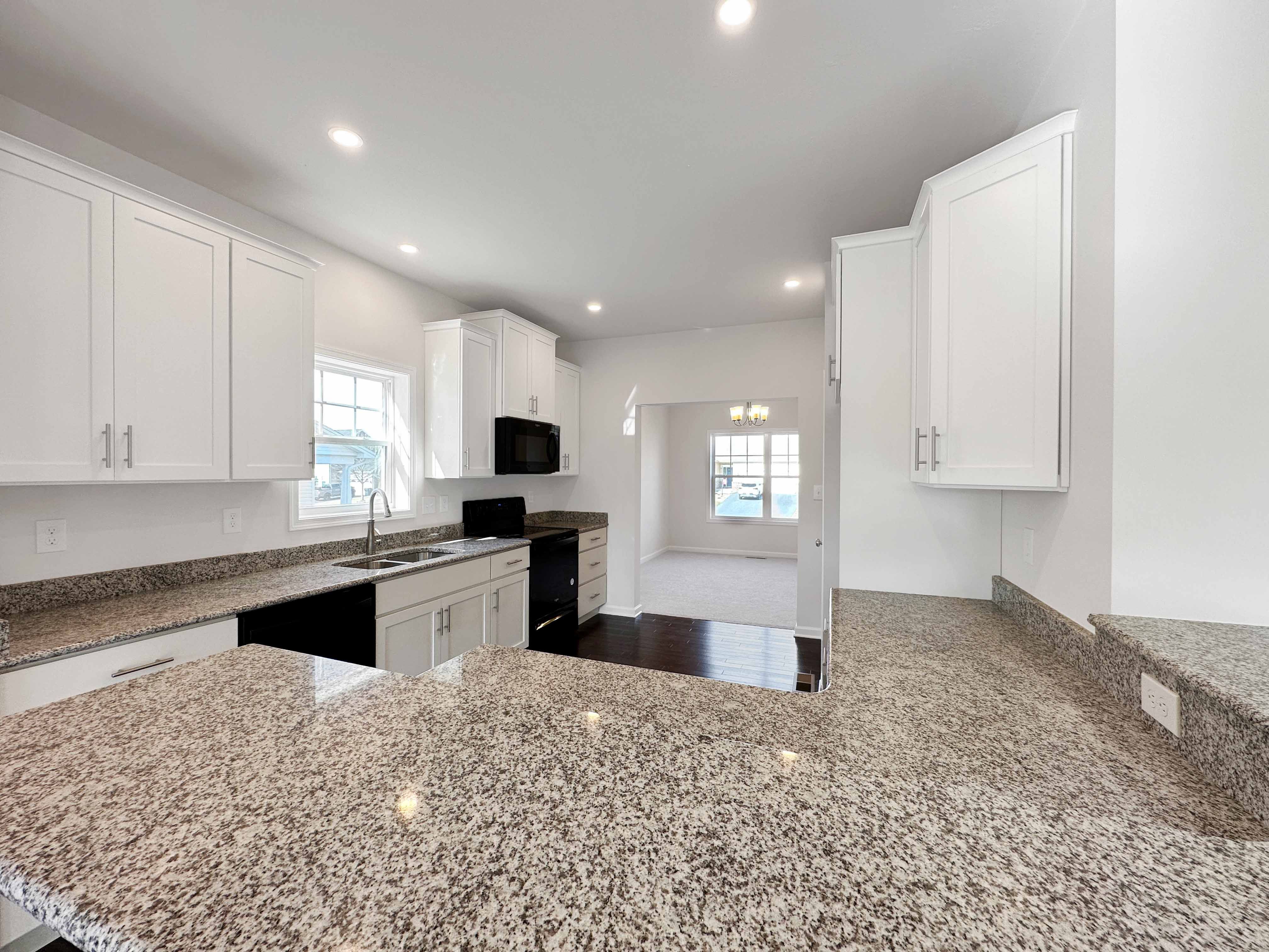 Kitchen with white cabinetry, granite countertops and black appliances.