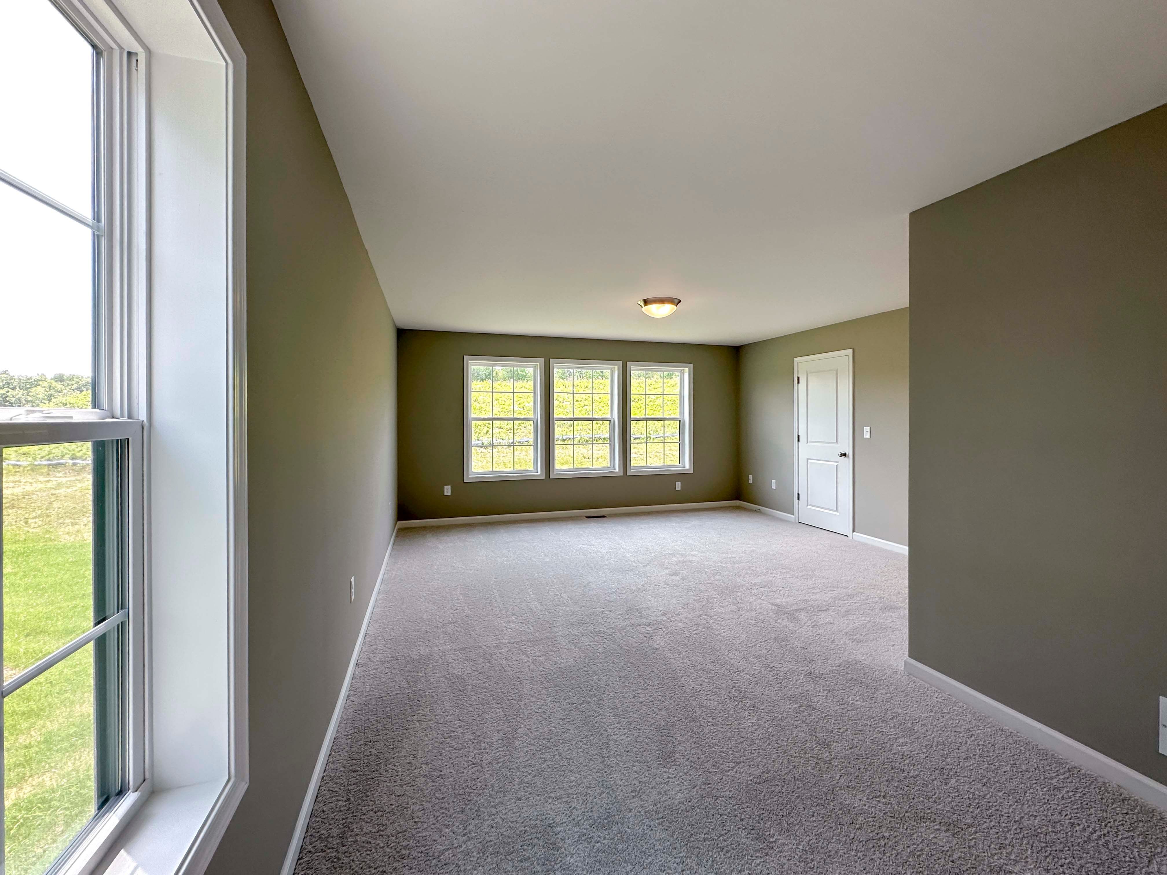 Unfurnished bedroom with carpet flooring and triple windows on rear wall