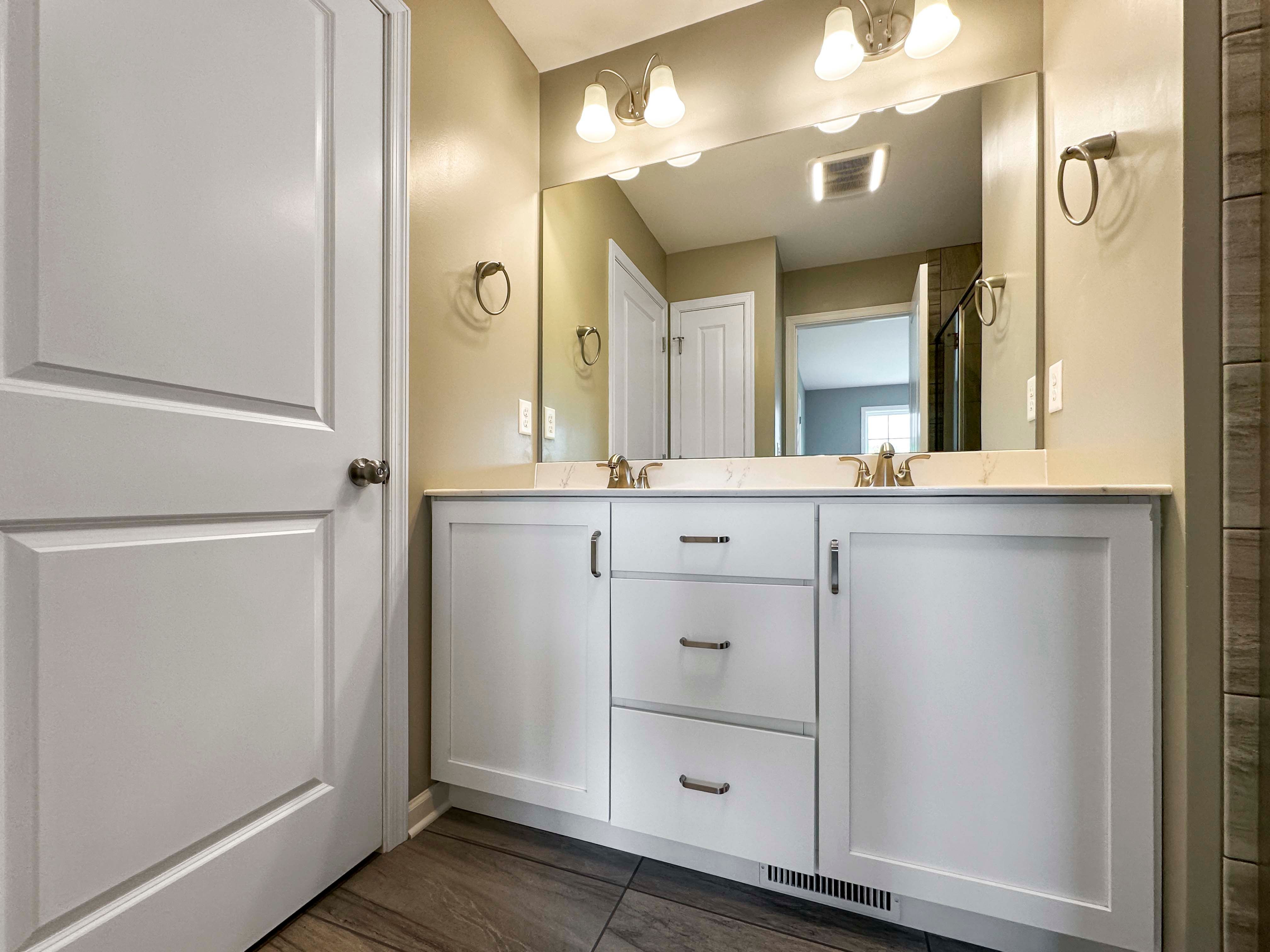 Bathroom with dual vanity, white cabinets, and large mirror above