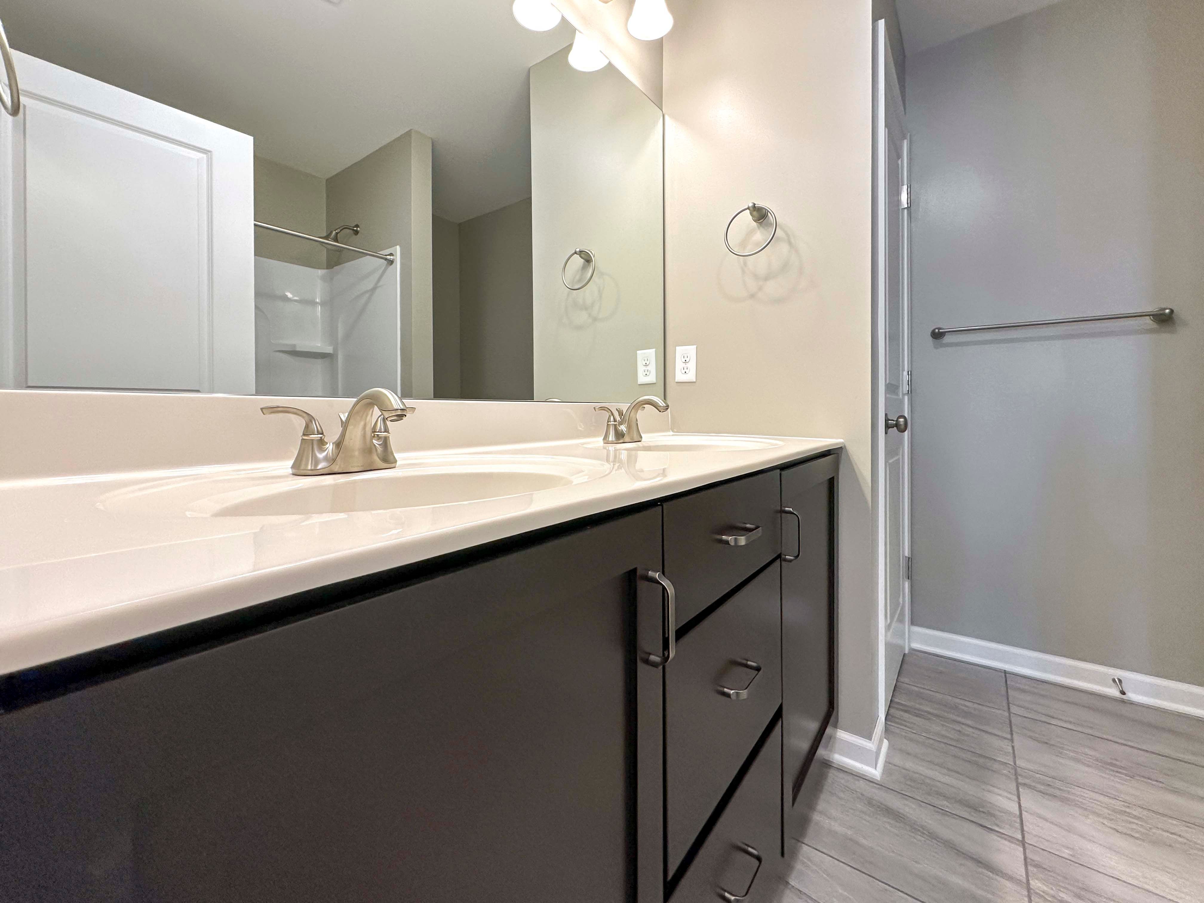 Bathroom with dual vanity, dark cabinets, and large mirror above