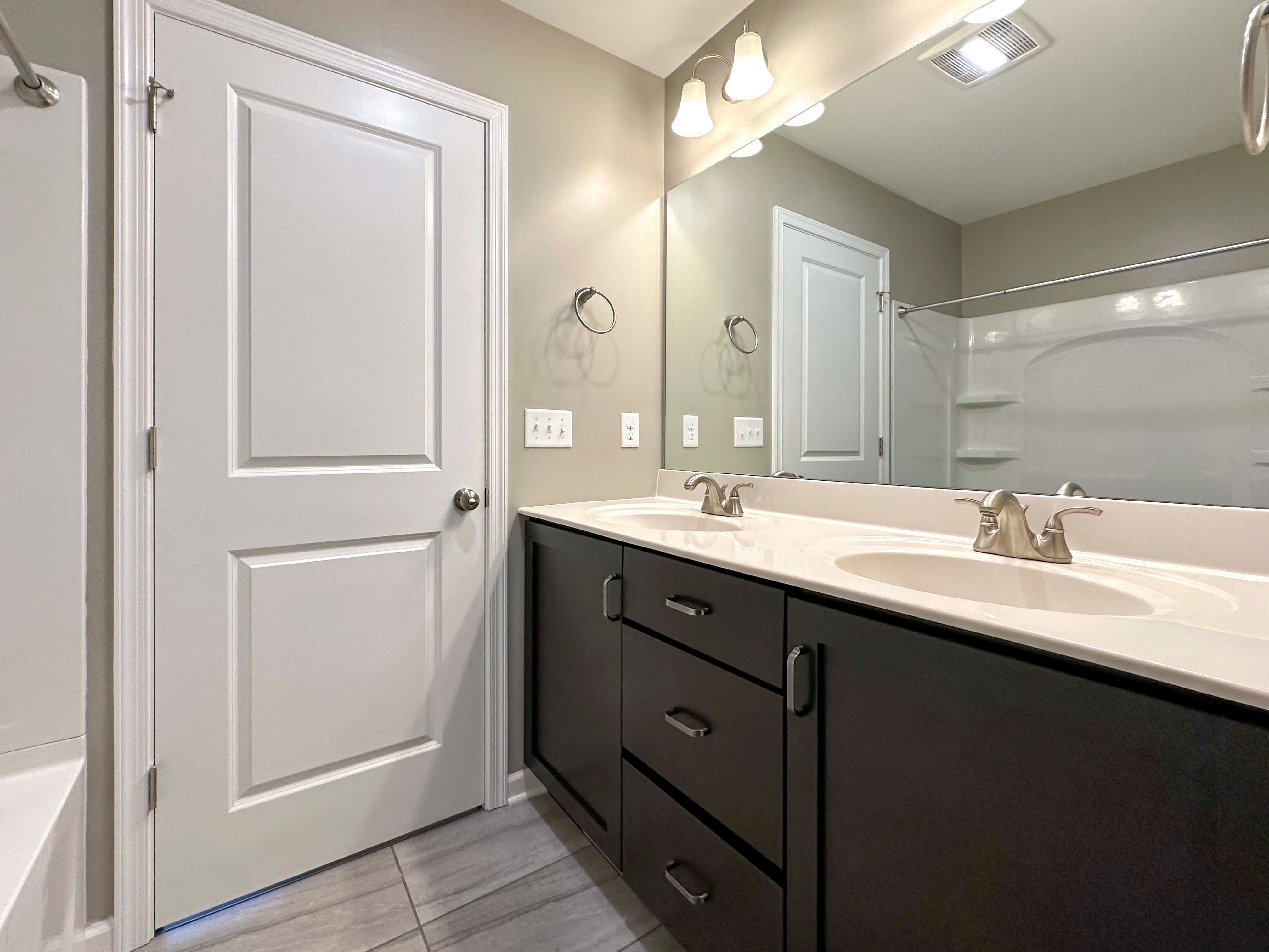 Bathroom with dual vanity, dark cabinets, and large mirror above