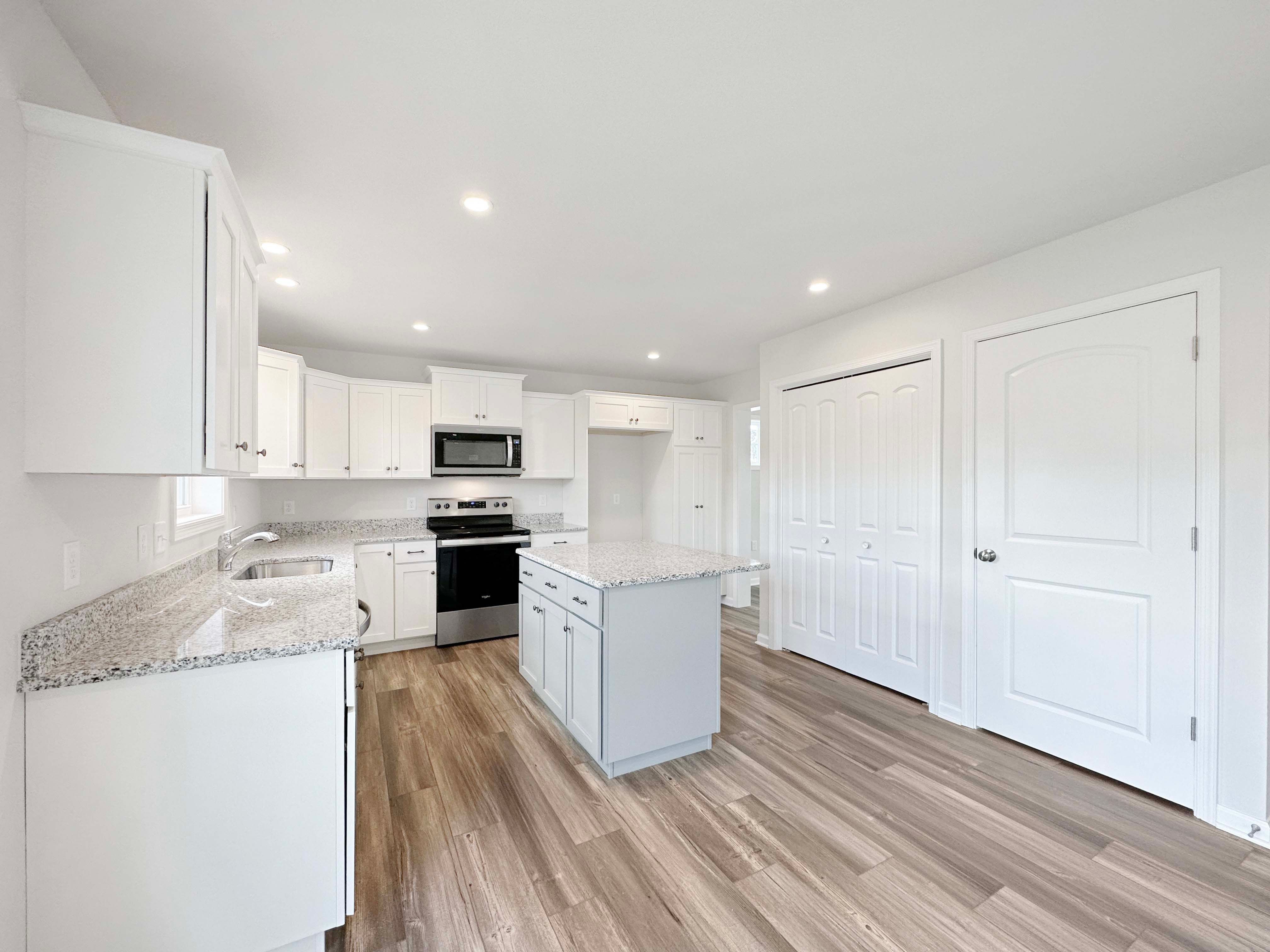 Kitchen with center island,white cabinetry, stainless appliances, and granite countertops. Entrance to basement stairs to right.