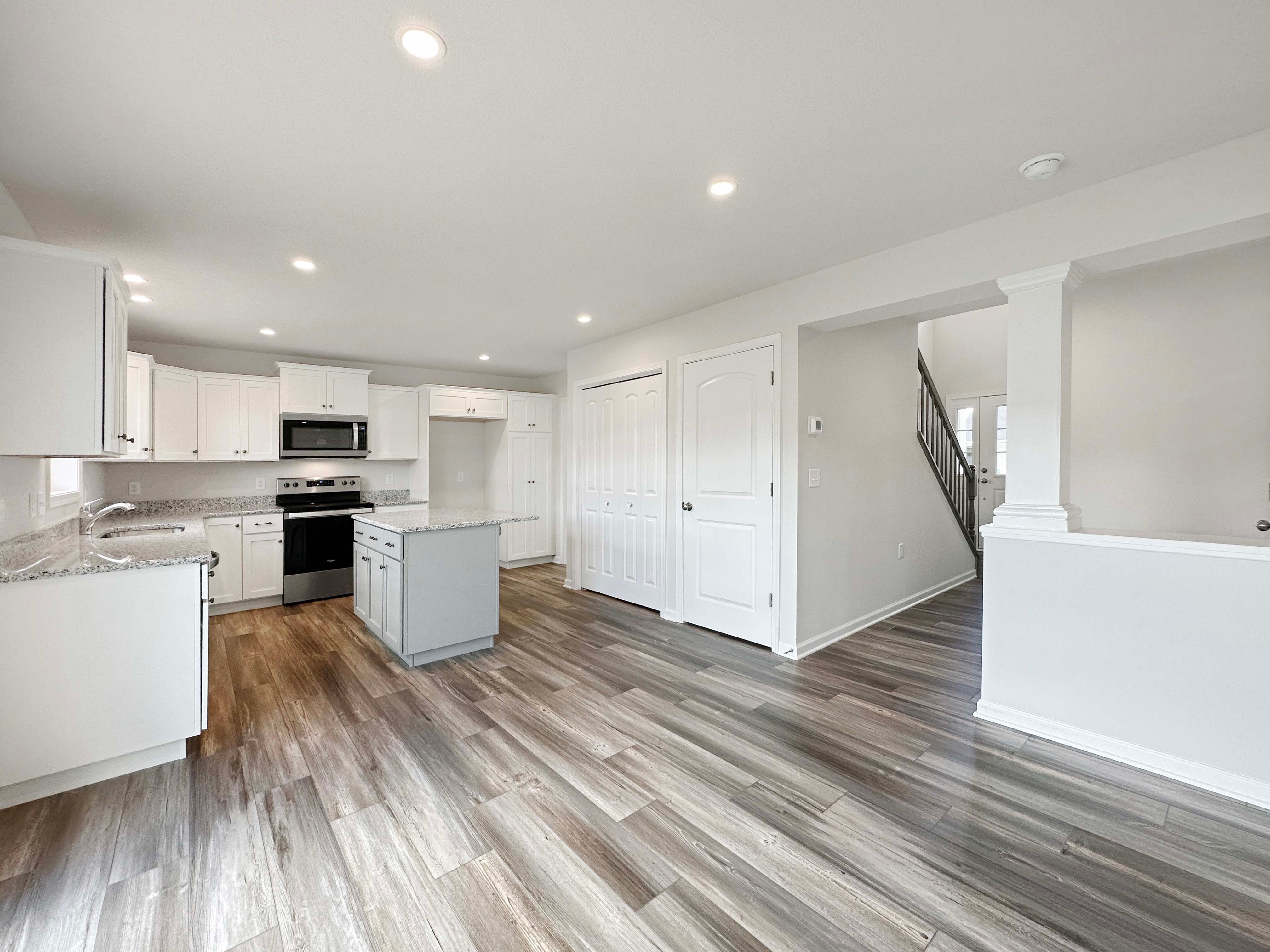 Kitchen with center island, white cabinetry, stainless appliances, and granite countertops. Entrance to basement stairs to right.