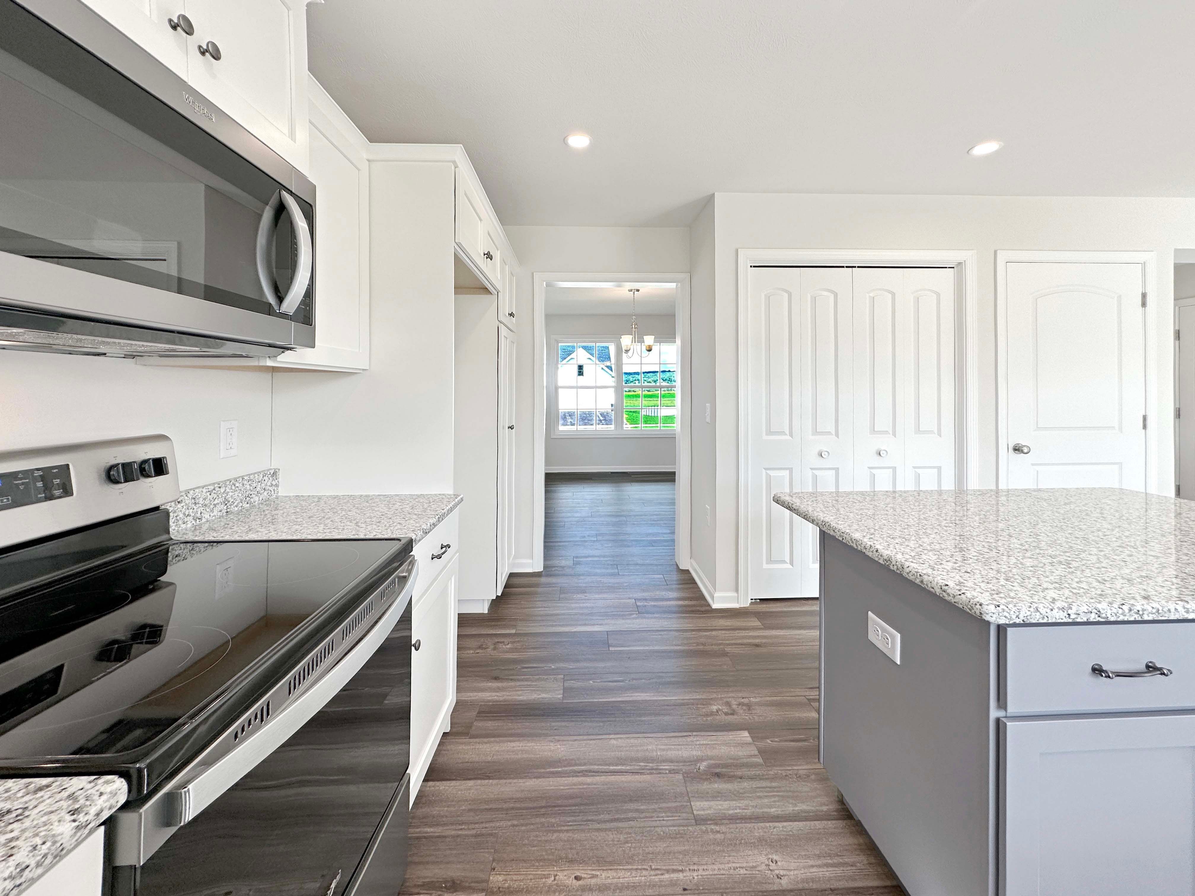 Kitchen with center island, white cabinetry, stainless appliances, and granite countertops. Facing pantry door and entrance to dining room in background.