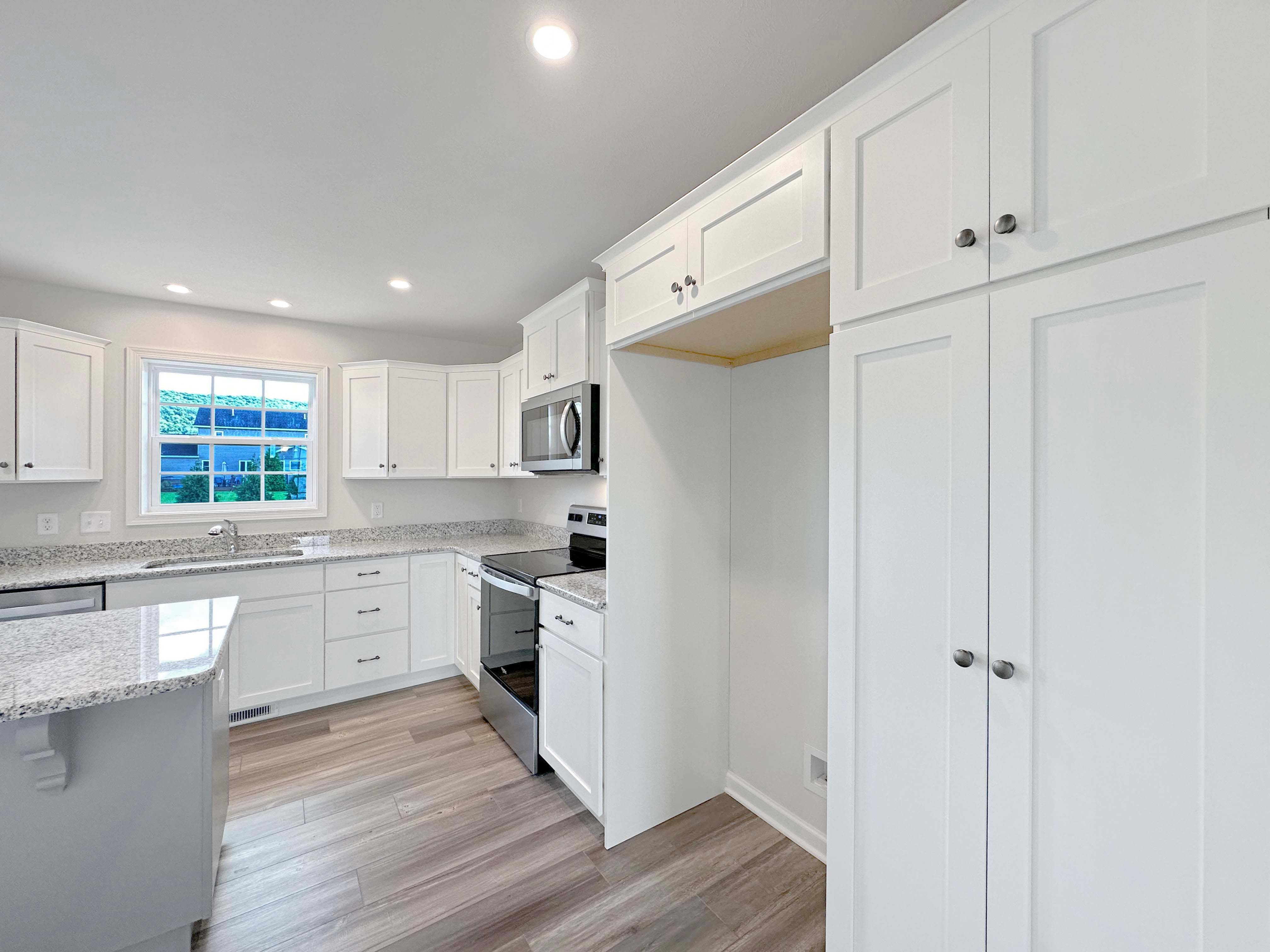 Kitchen with center island, white cabinetry, stainless dishwasher, and granite countertops. Window above kitchen sink.
