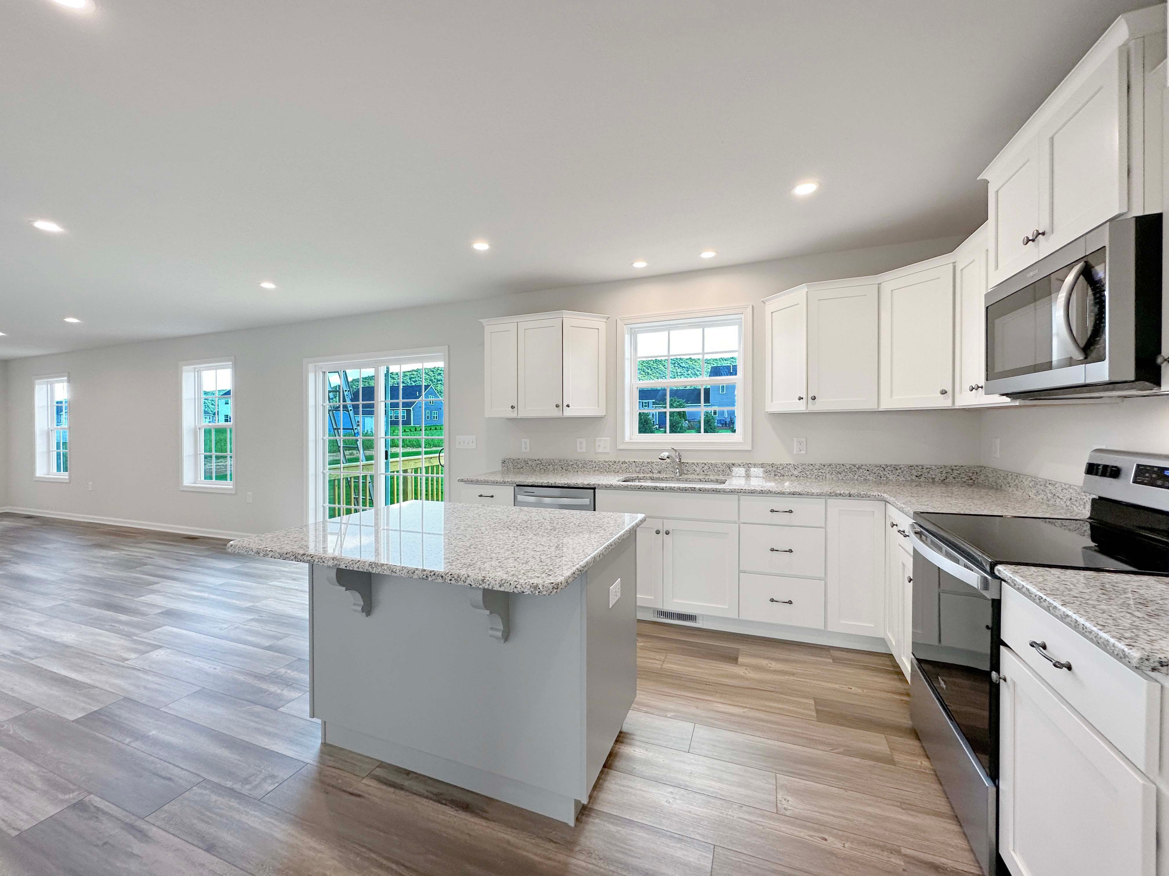 Kitchen with center island, white cabinetry, stainless dishwasher, and granite countertops. Window above kitchen sink and sliding glass door at edge of kitchen.