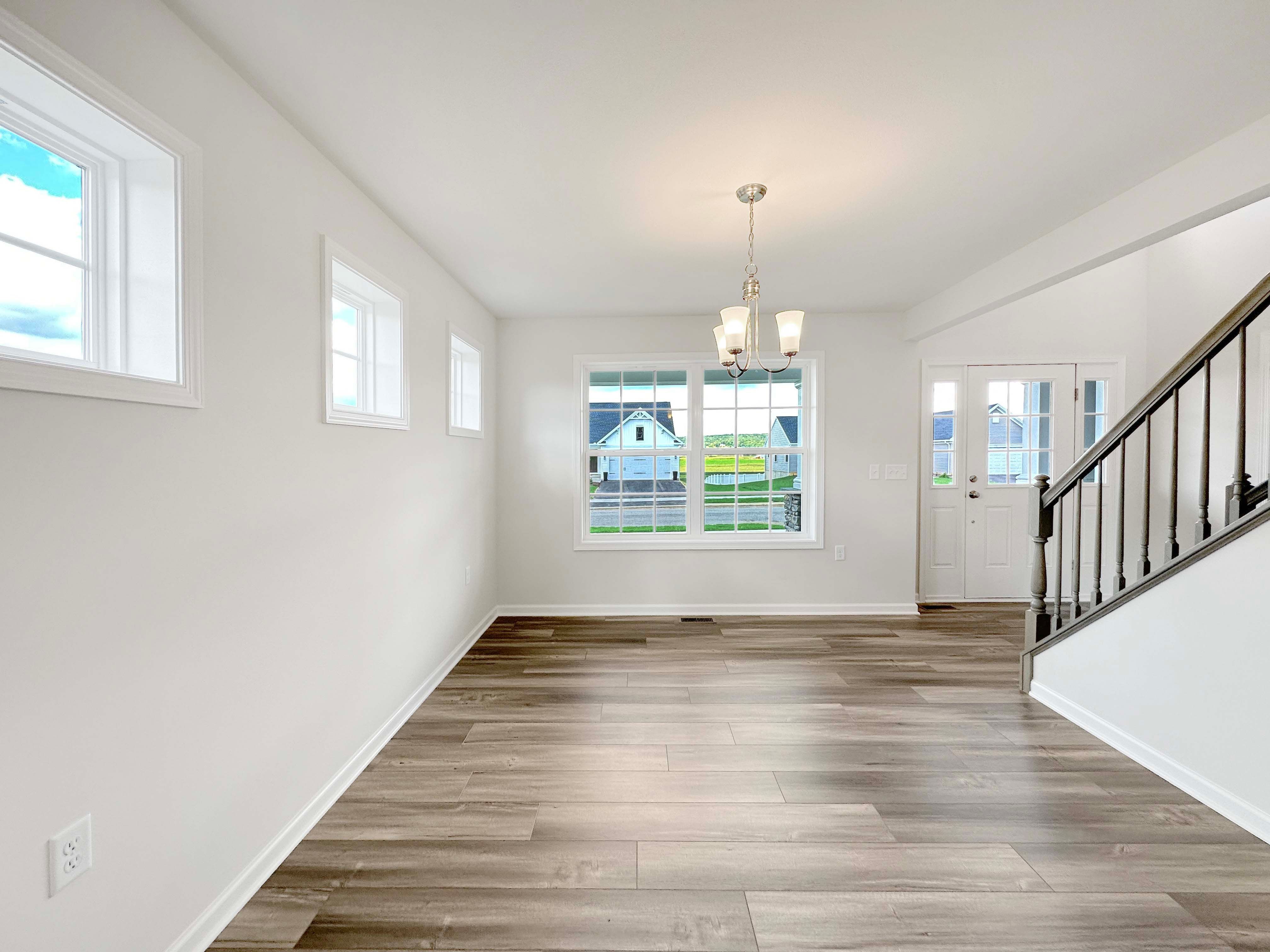 Dining Room with pendant light and LVT flooring. 3 windows on the left wall, one double pane window on the rear wall, and the entryway / foyer to the right.