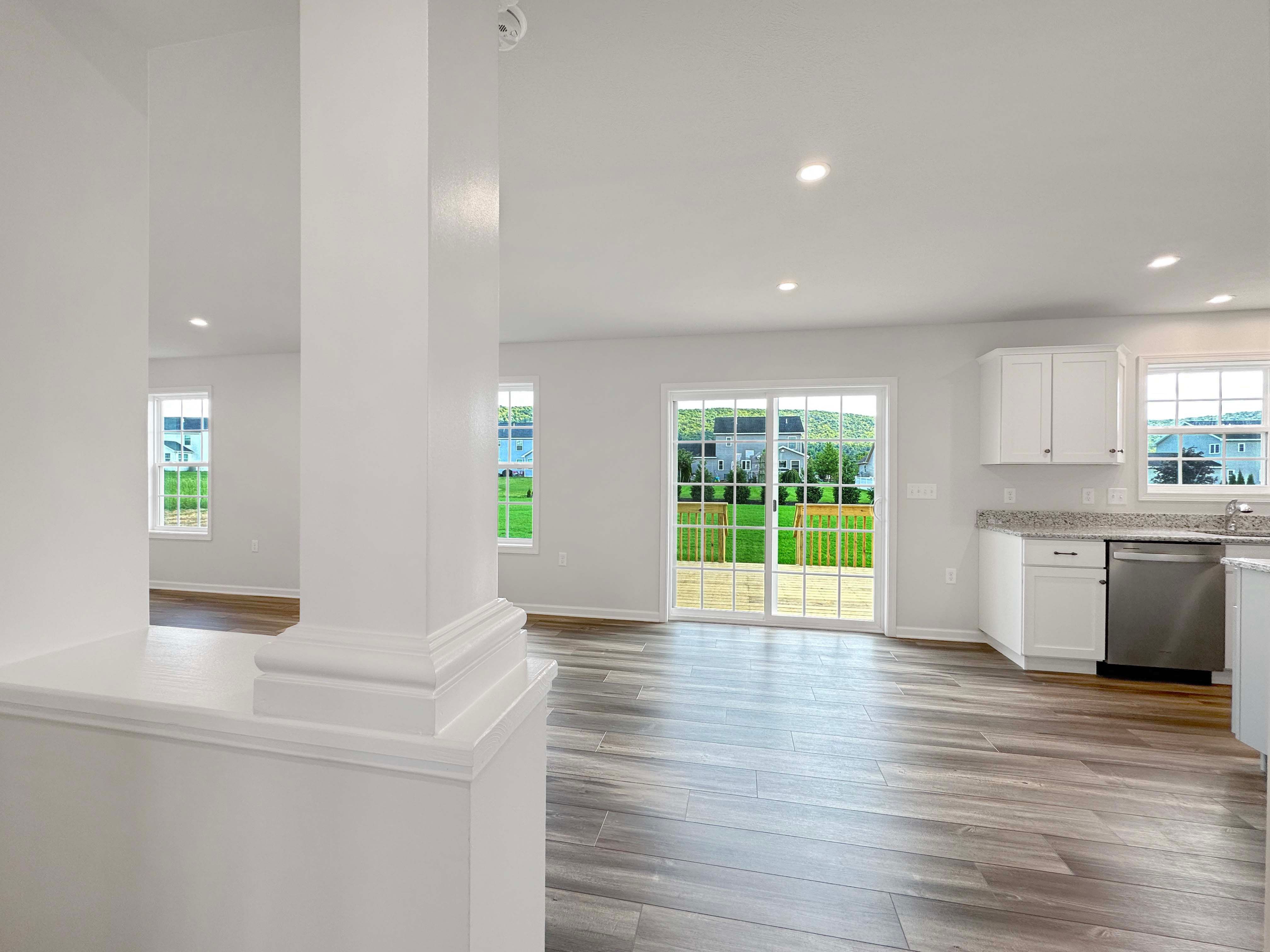 Hallway into Family Room and Kitchen area - sliding glass door to patio on rear wall. Kitchen on right side with white cabinetry and stainless appliances.