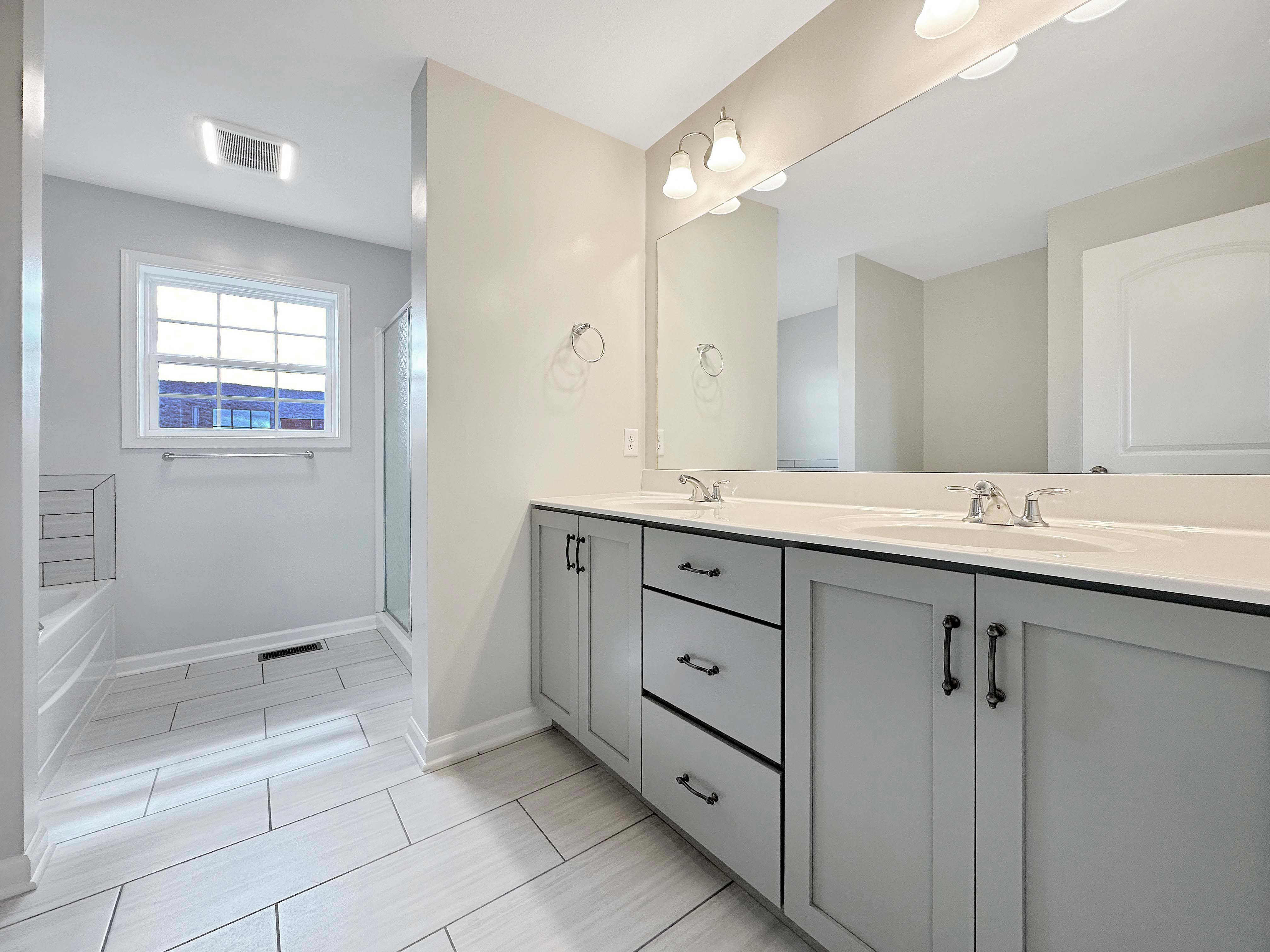 Owner's bathroom with ceramic tile flooring, grey cabinetry, soaking tub, walk-in tile shower, and double vanity.