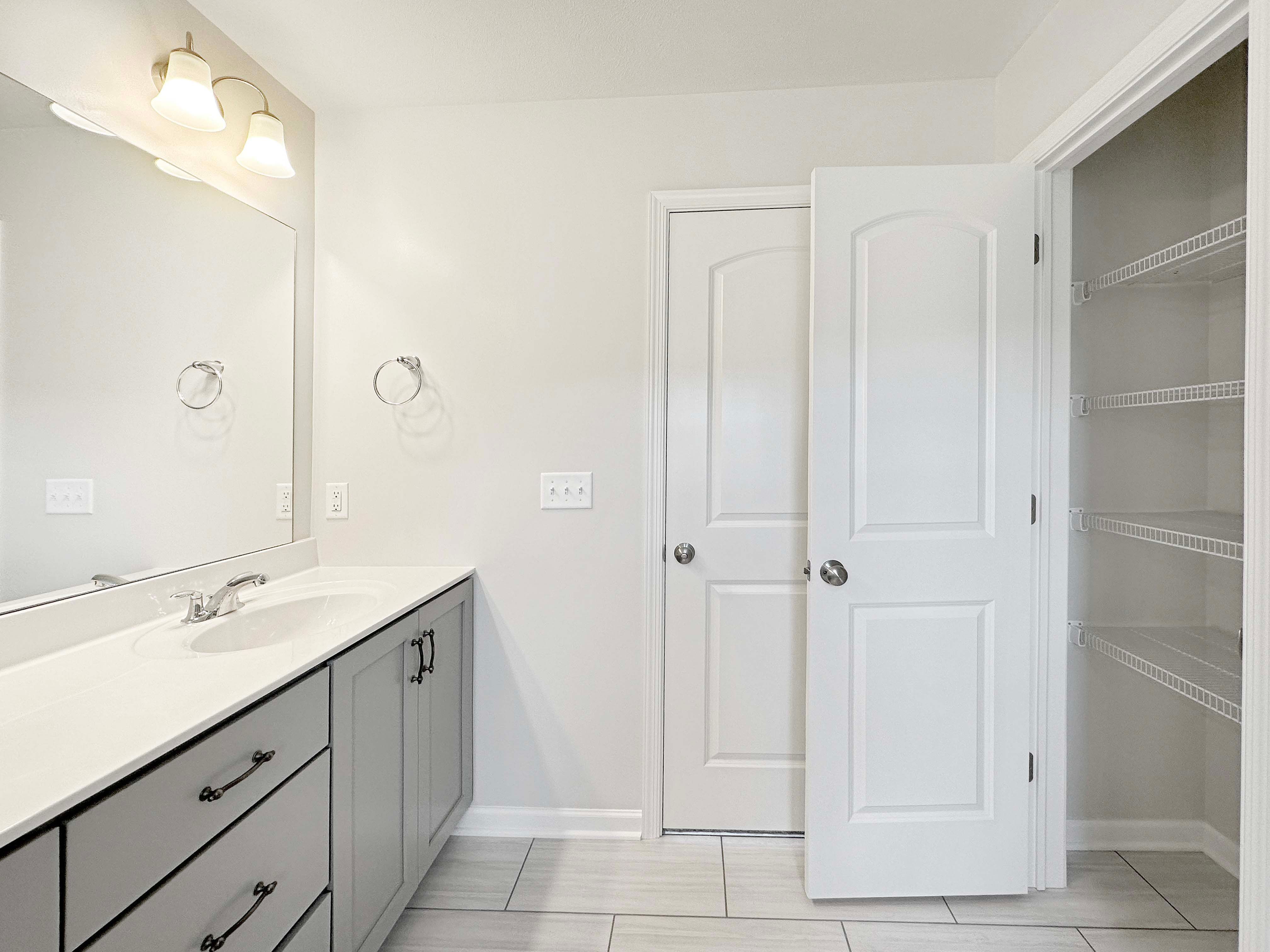Owner's bathroom with linen closet, double vanity, grey cabinetry, and ceramic tile flooring.