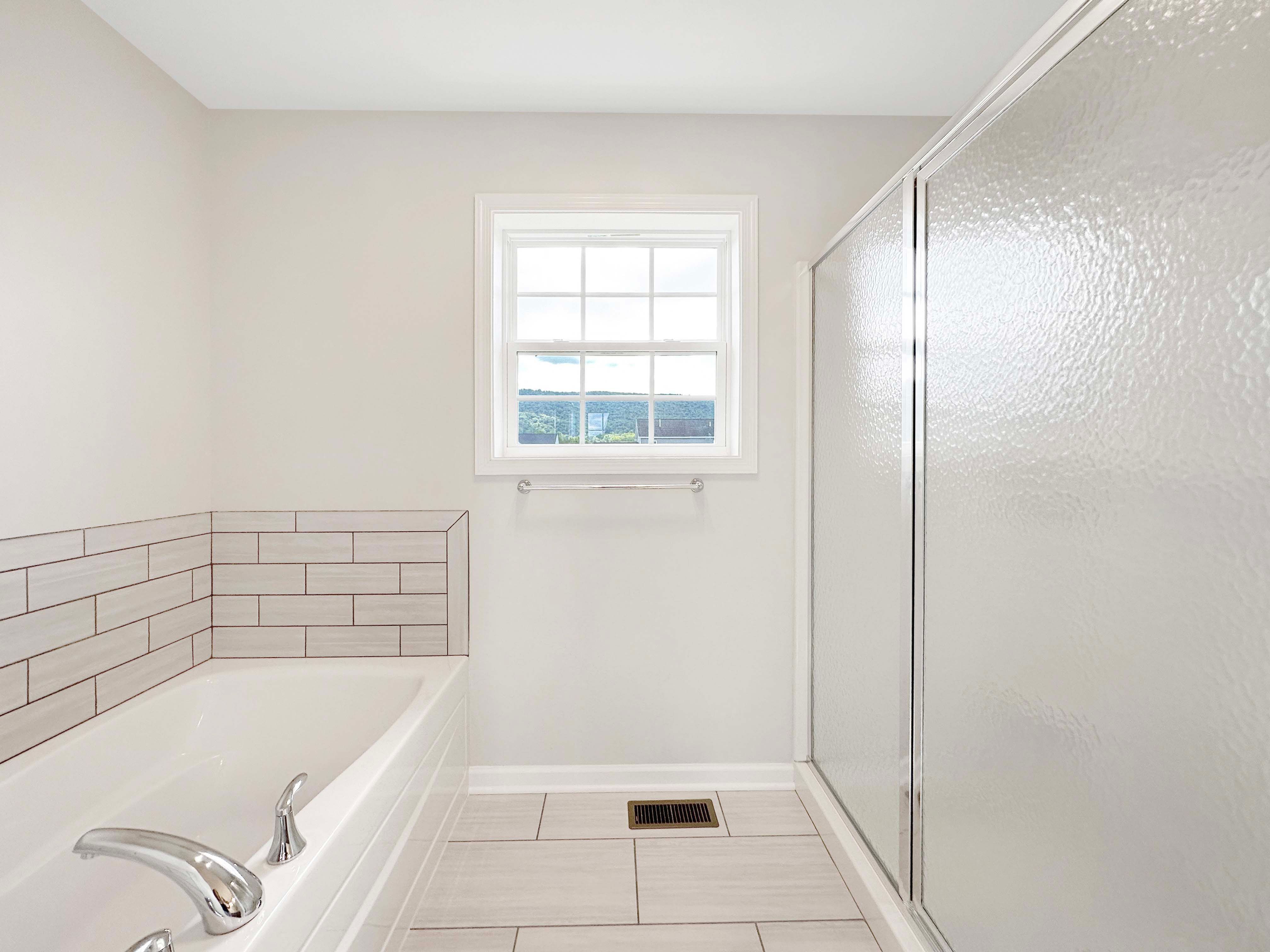 Owner's bathroom with ceramic tile flooring, and soaking tub with tile accent wall across from walk-in tile shower with sliding glass doors.