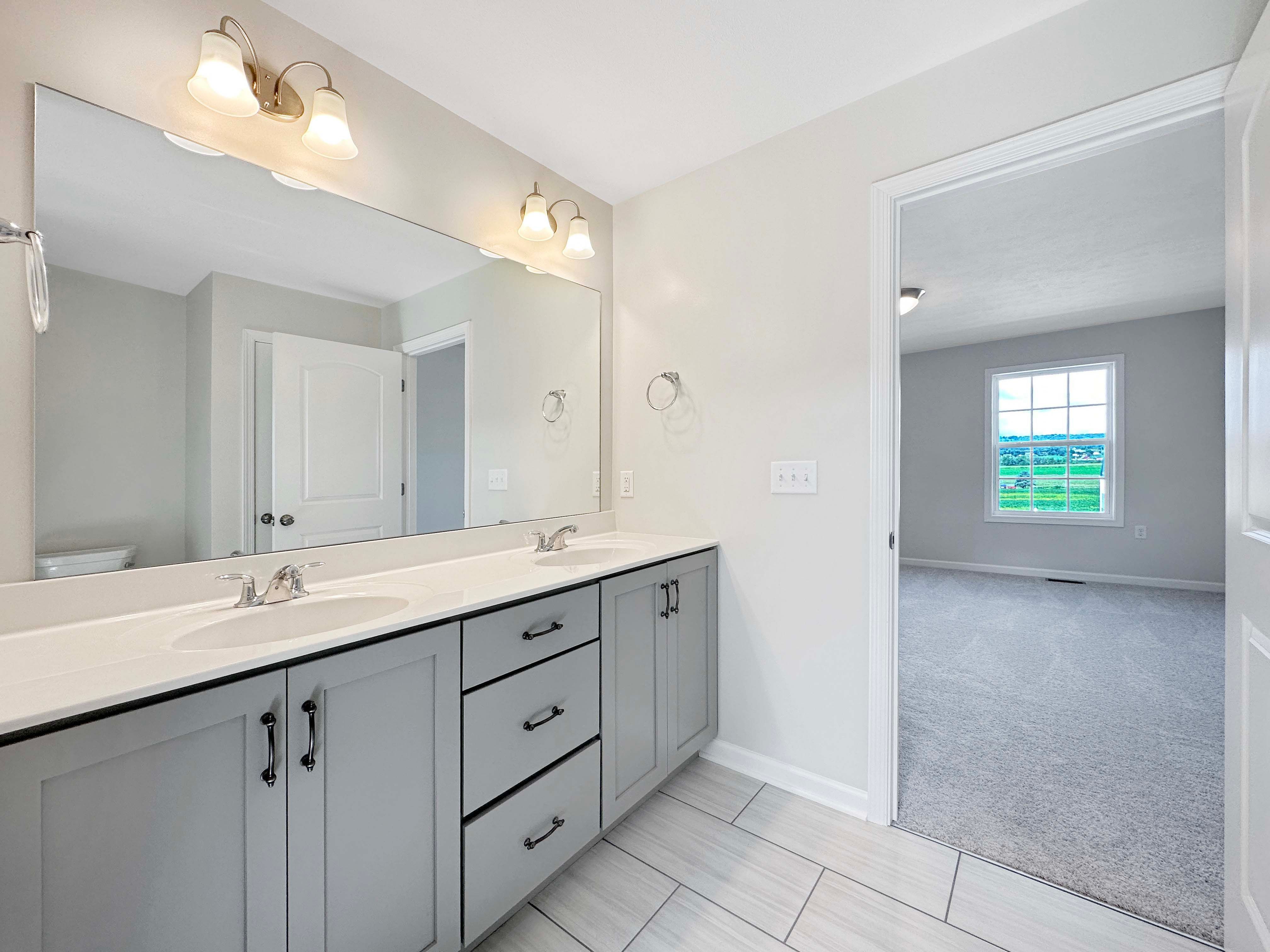 Owner's bathroom with ceramic tile flooring and grey cabinetry, door to Owner's bedroom - window on wall in background.