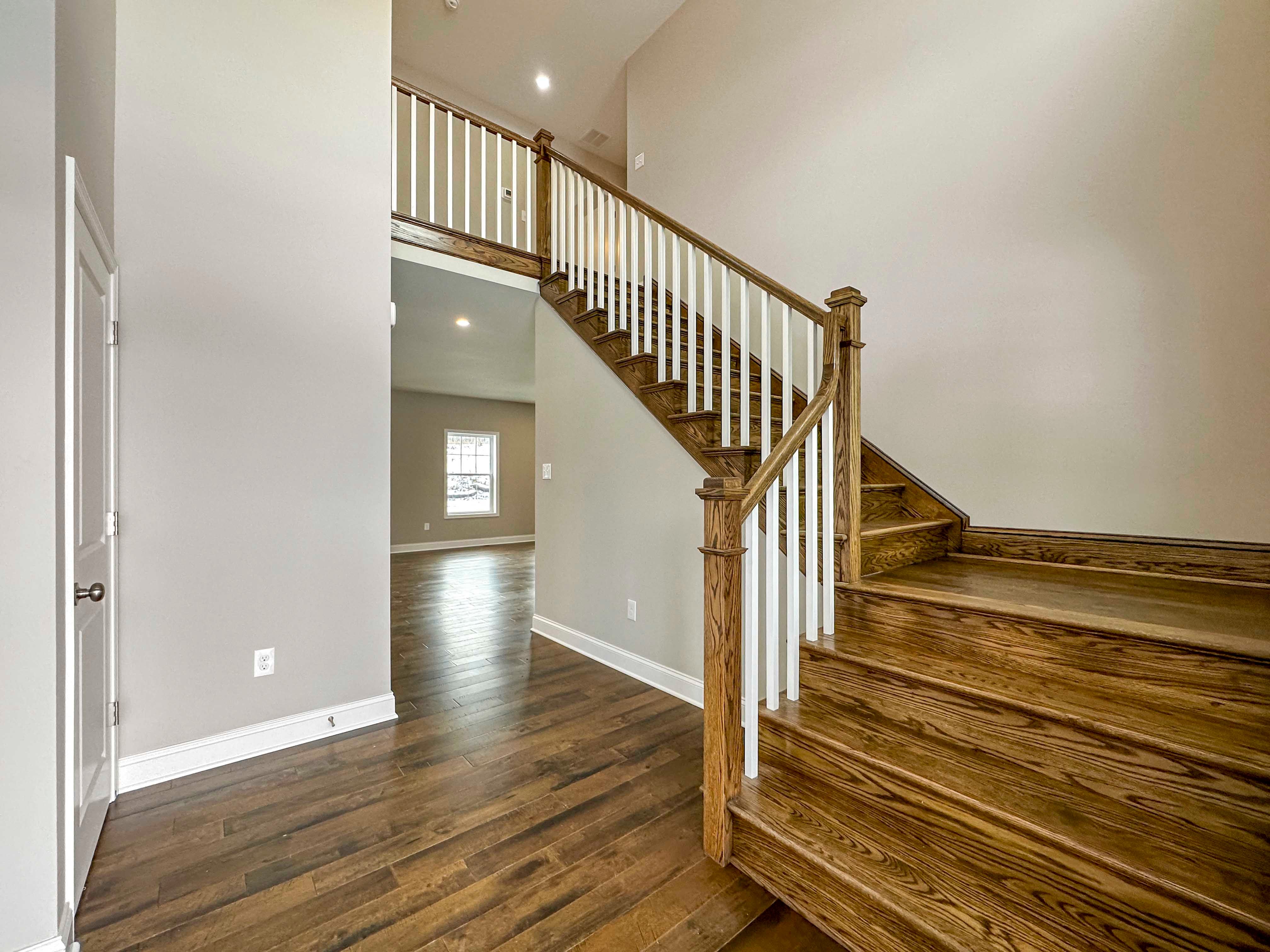 Foyer - staircase to right with hardwood floors, door to powder room to left, window on rear wall of Family Room in background.