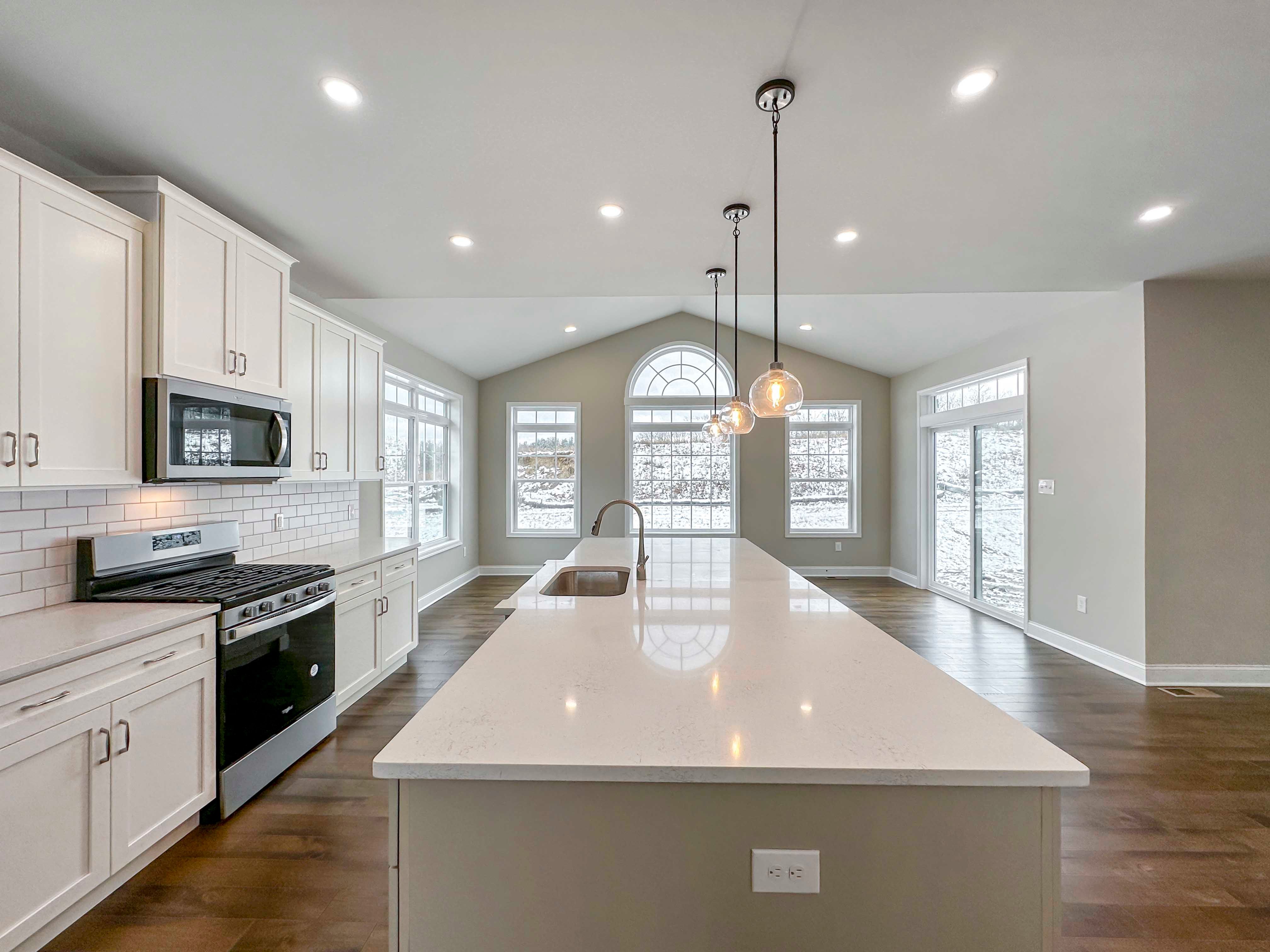 Kitchen - Luxury Kitchen with white cabinetry, white countertops, tile backsplash, island with sink and overhead pendant lighting, and stainless appliances - with the Opt. Keeping Room in the rear.