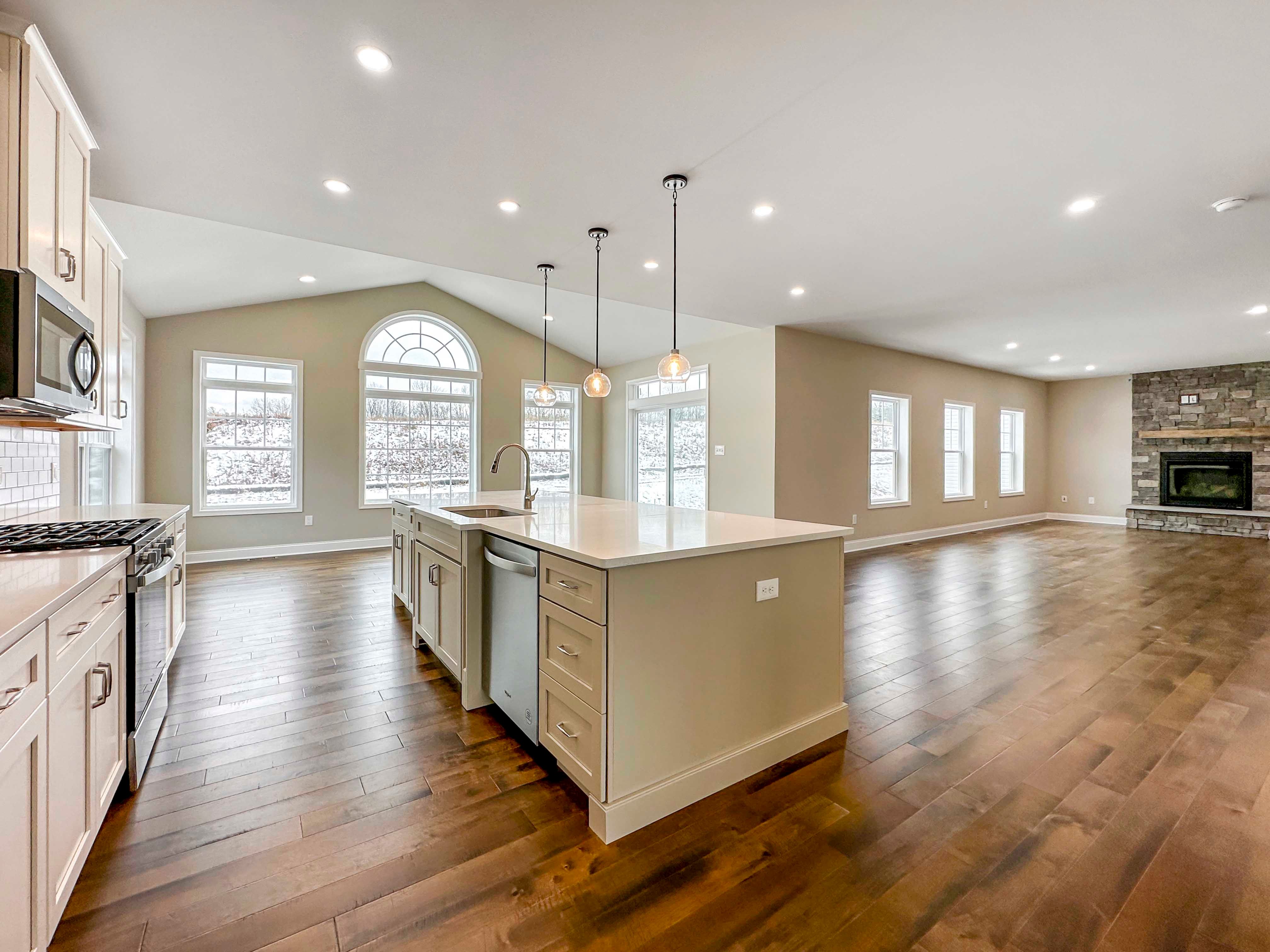 Kitchen - Luxury Kitchen with white cabinetry, white countertops, tile backsplash, island with sink and overhead pendant lighting, and stainless appliances - with the Opt. Keeping Room in the rear on the left and Family Room on the right.