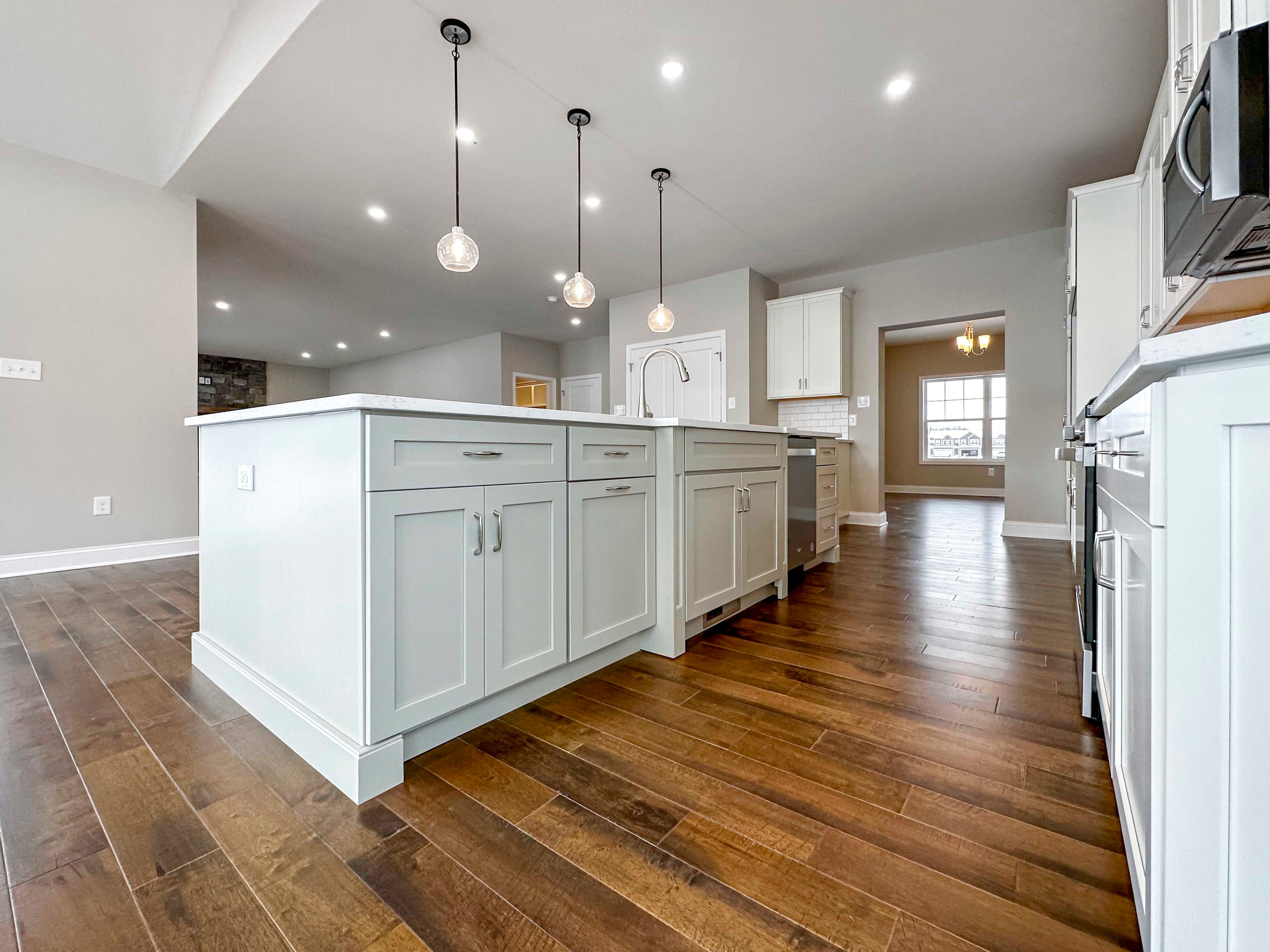 Kitchen Island - Upgraded pendant lighting overhead, white cabinetry, hardwood flooring, stainless appliances, and access to Formal Dining Room to rear.