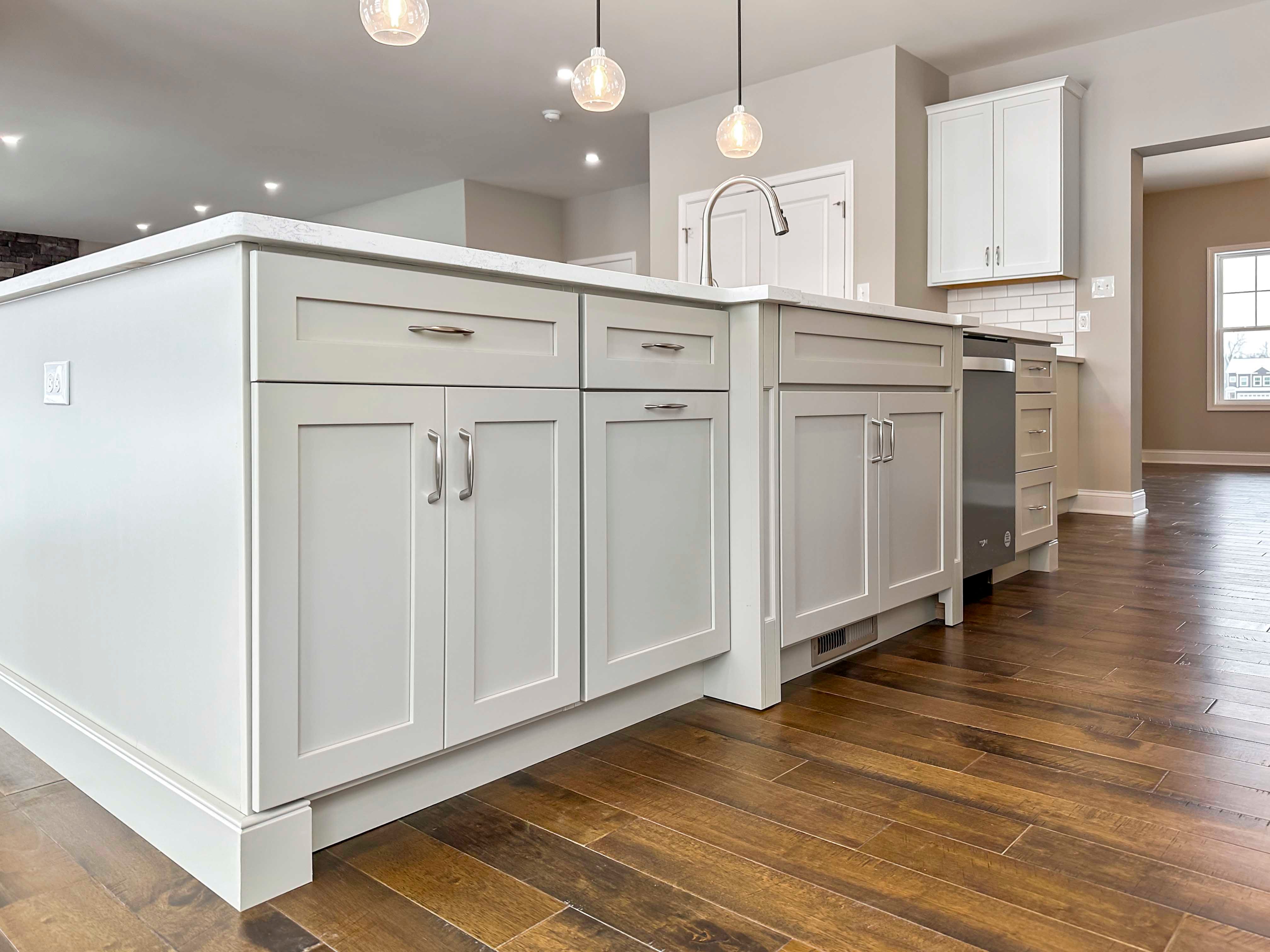 Kitchen Island - Upgraded pendant lighting overhead, white cabinetry, hardwood flooring, stainless appliances, and access to Formal Dining Room to rear.