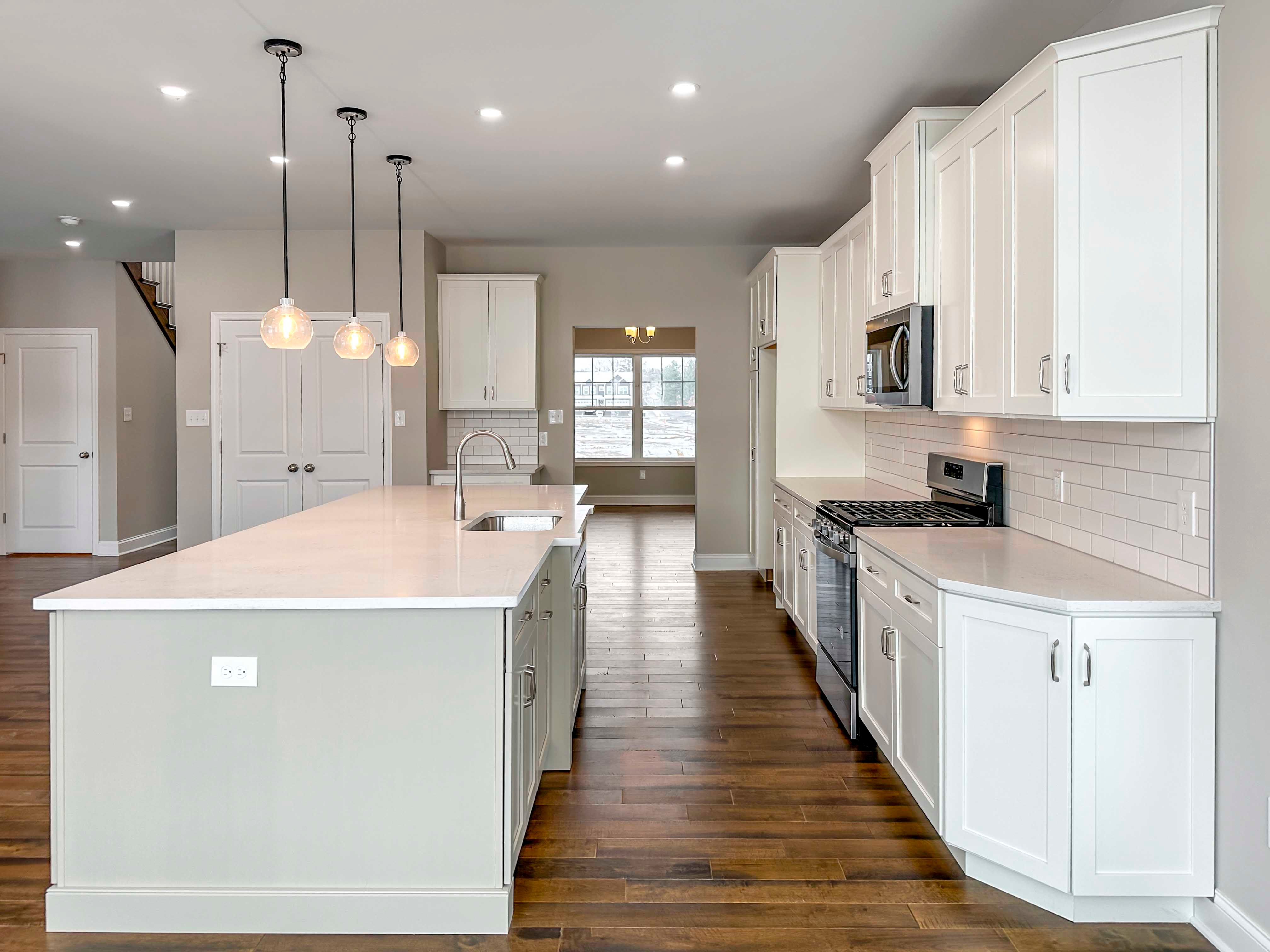 Kitchen - Luxury Kitchen with white cabinetry, white countertops, tile backsplash, island with sink and overhead pendant lighting, and stainless appliances, drop zone and pantry to the left - with the Formal Dining Room in the rear.