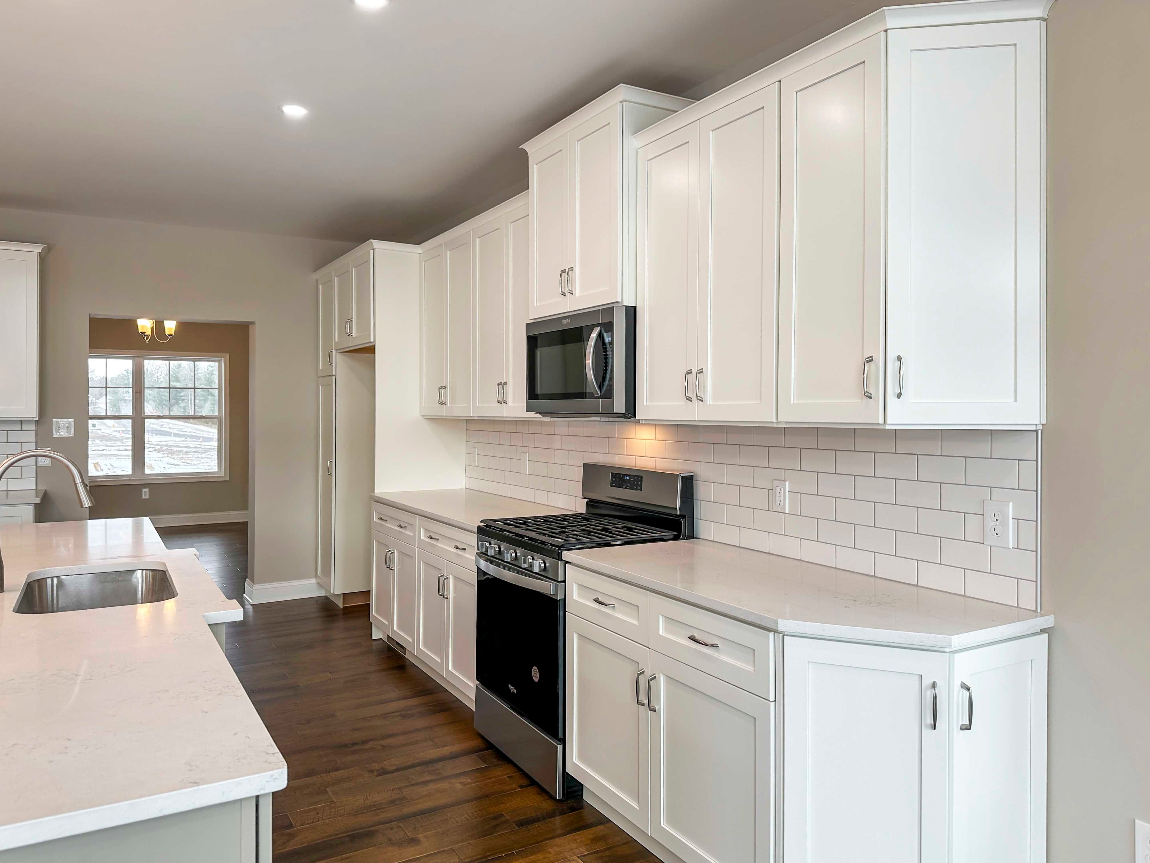Kitchen - Luxury Kitchen with white cabinetry, white countertops, tile backsplash, island with sink, and stainless appliances, with the Formal Dining Room in the rear.