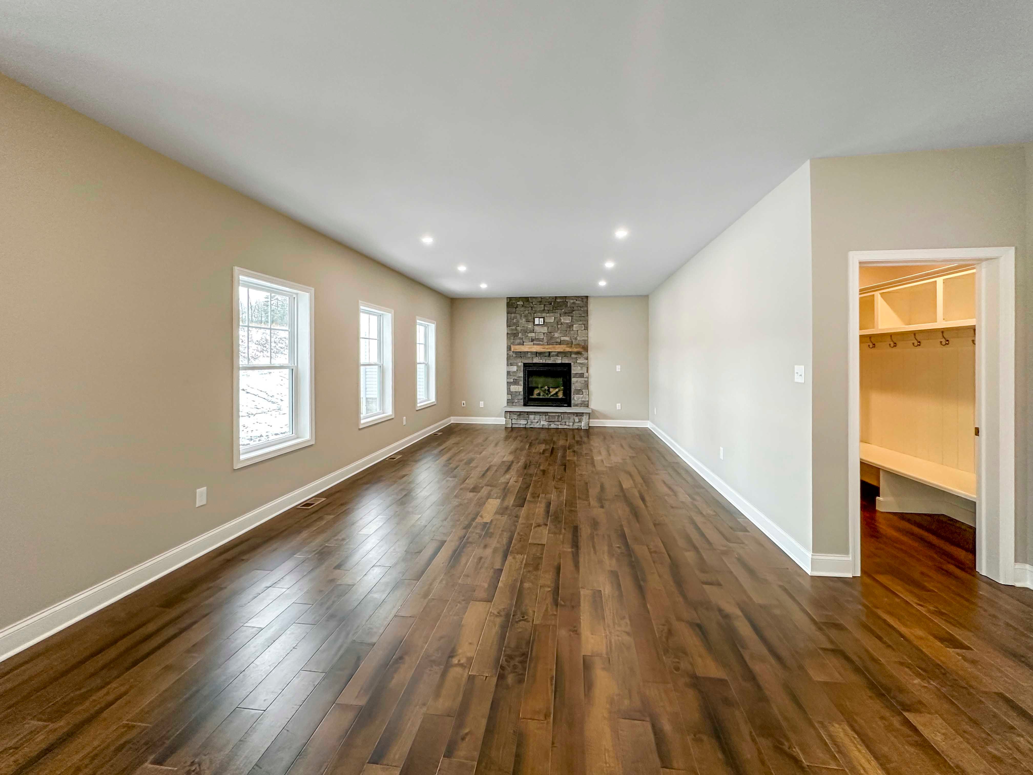 Family Room with three single-hung windows on wall to left and Fireplace with wood mantle and overhead recessed lighting lighting. Entrance to Mud Room to right.