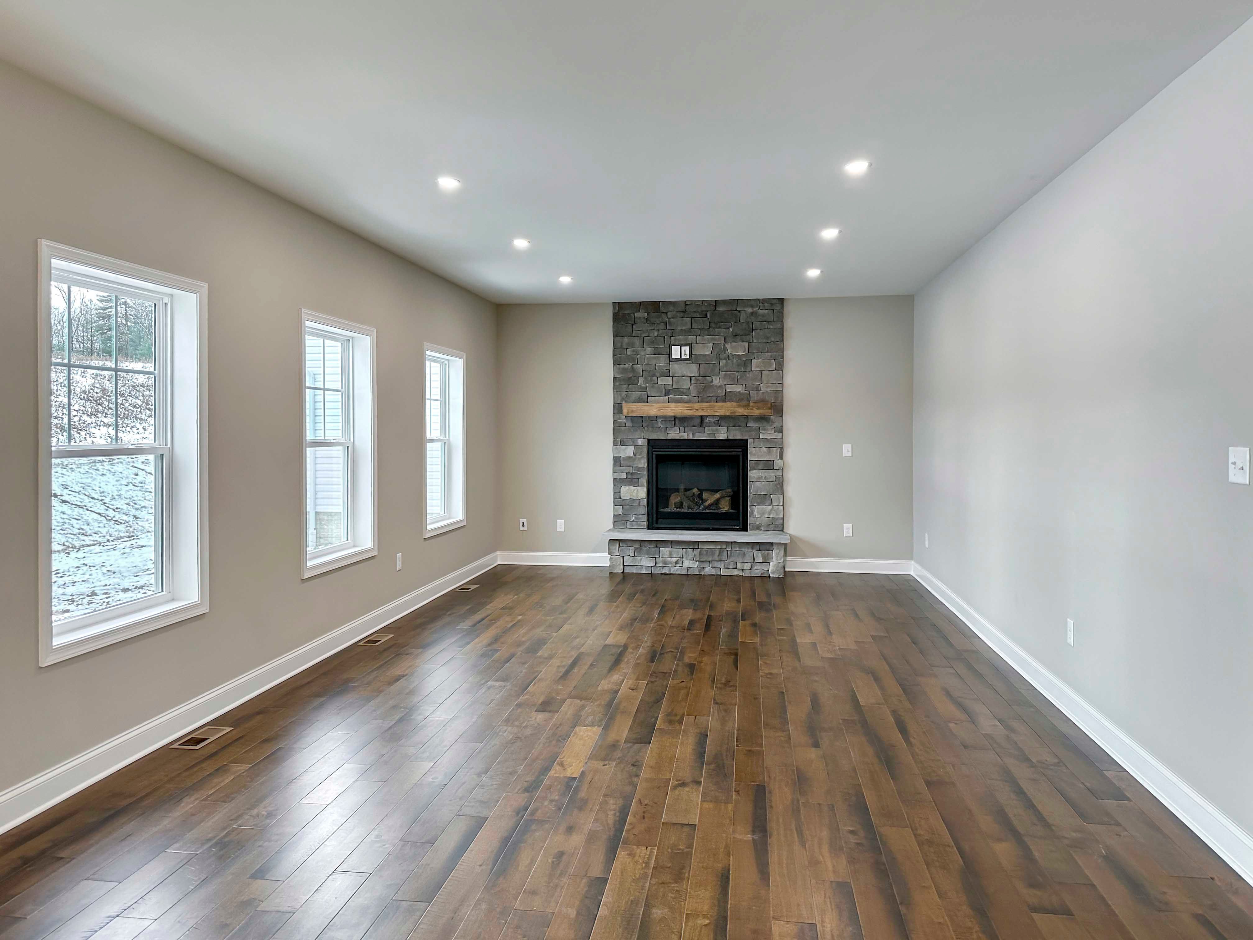 Family Room with three single-hung windows on wall to left and Fireplace with wood mantle and overhead recessed lighting lighting.