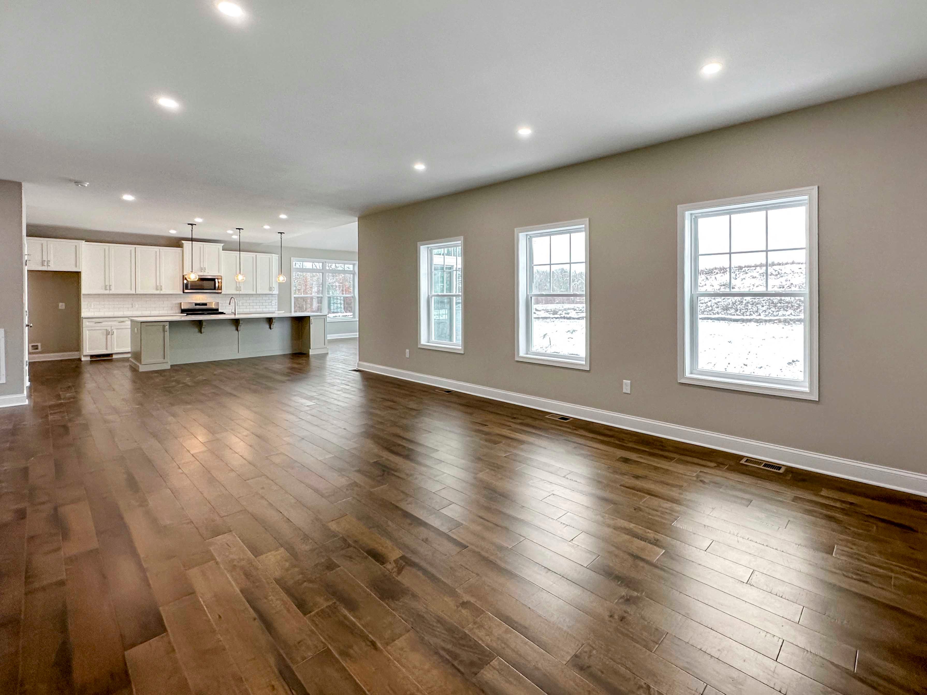 Family Room with three single hung windows to right. Hardwood floors and recessed lighting, onlooking kitchen.
