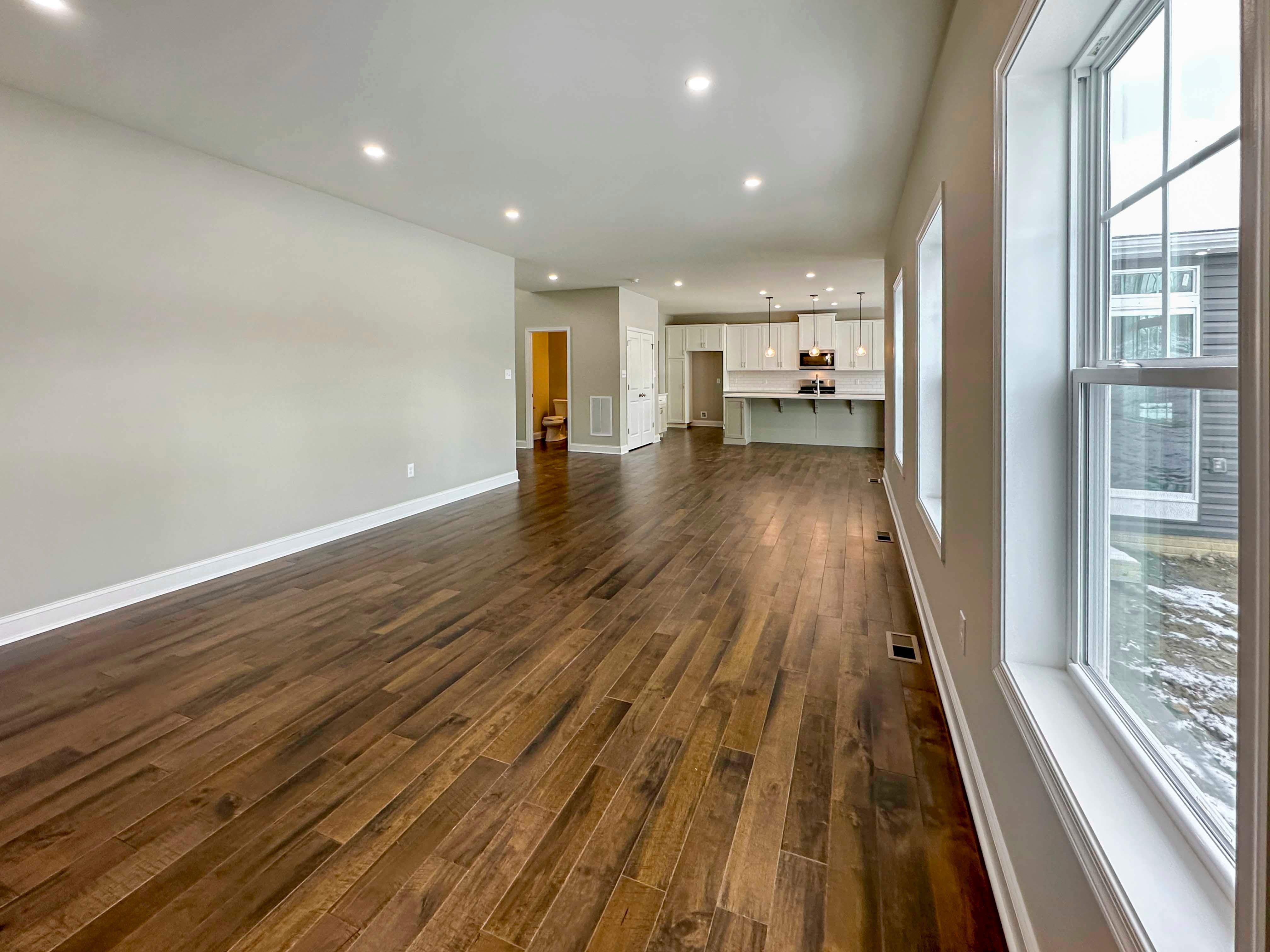 Family Room with three single hung windows to right. Hardwood floors and recessed lighting, onlooking kitchen. Door to Powder Room on far left.