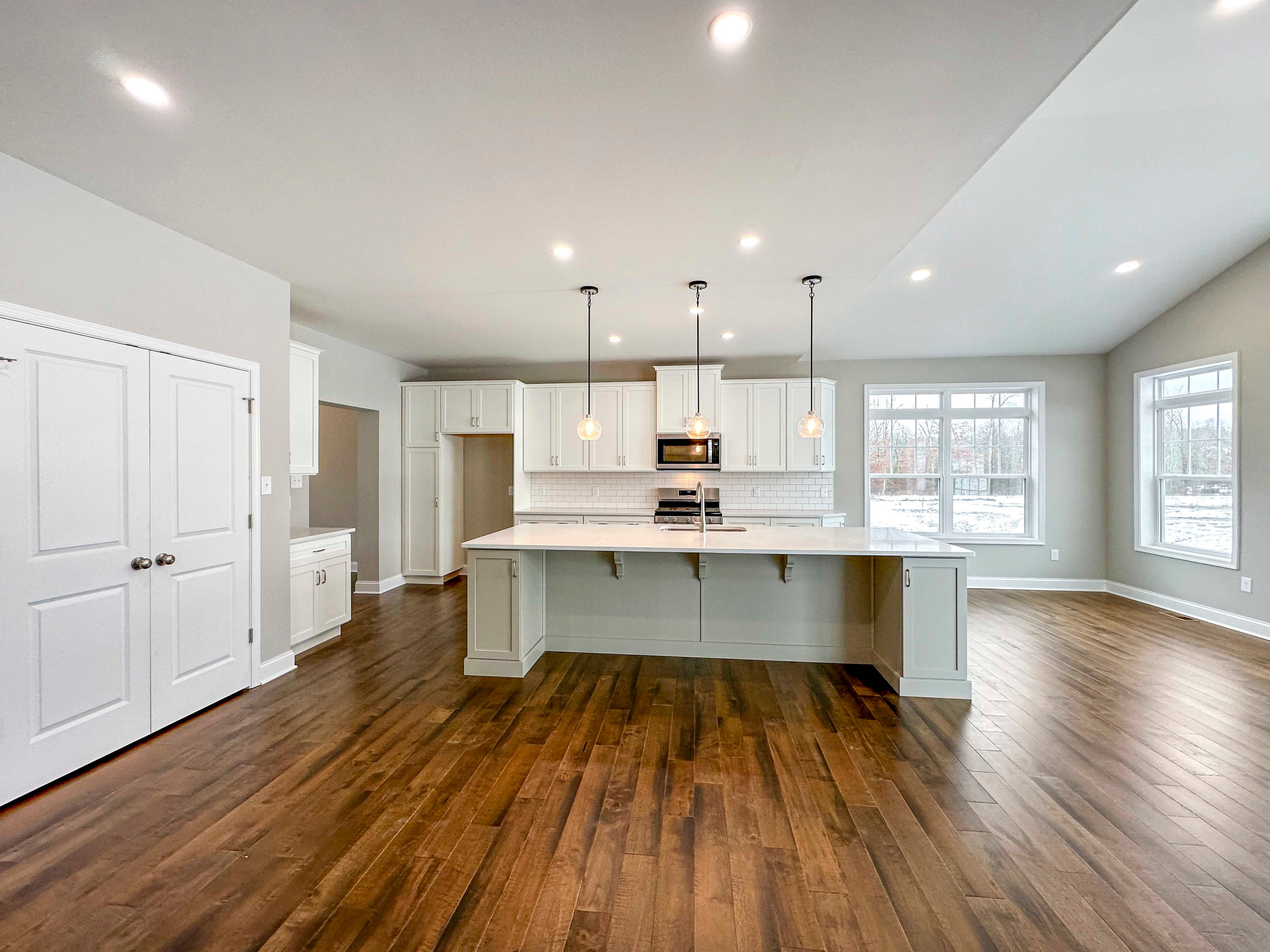 Kitchen - Island with overhang, white cabinetry, and hardwood floor - Pantry doors on left,Opt. Keeping Room to right.
