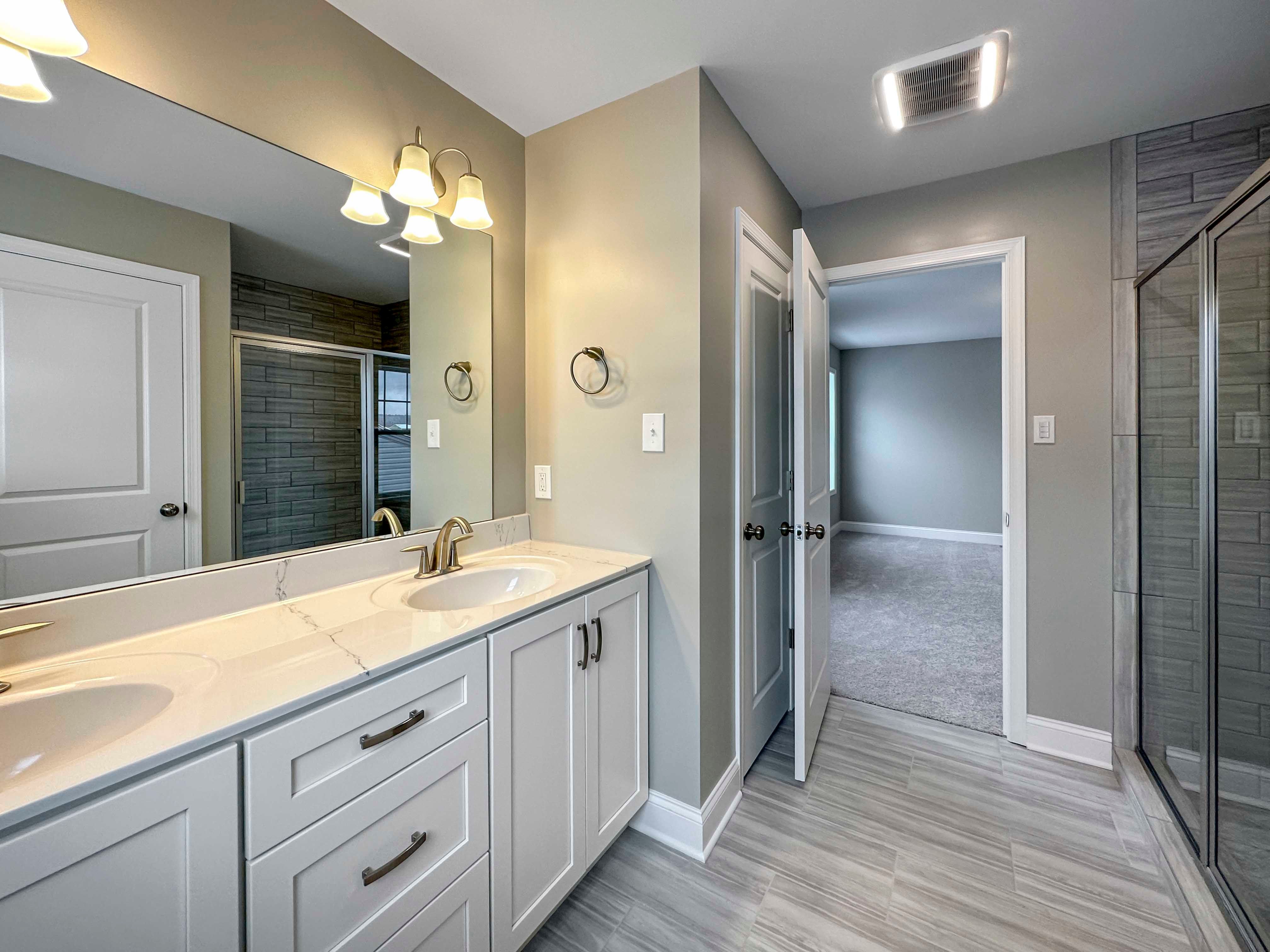 Owner's Bathroom - double vanity with white cabinetry, linen closet, walk-in ceramic tile shower with glass doors to right.