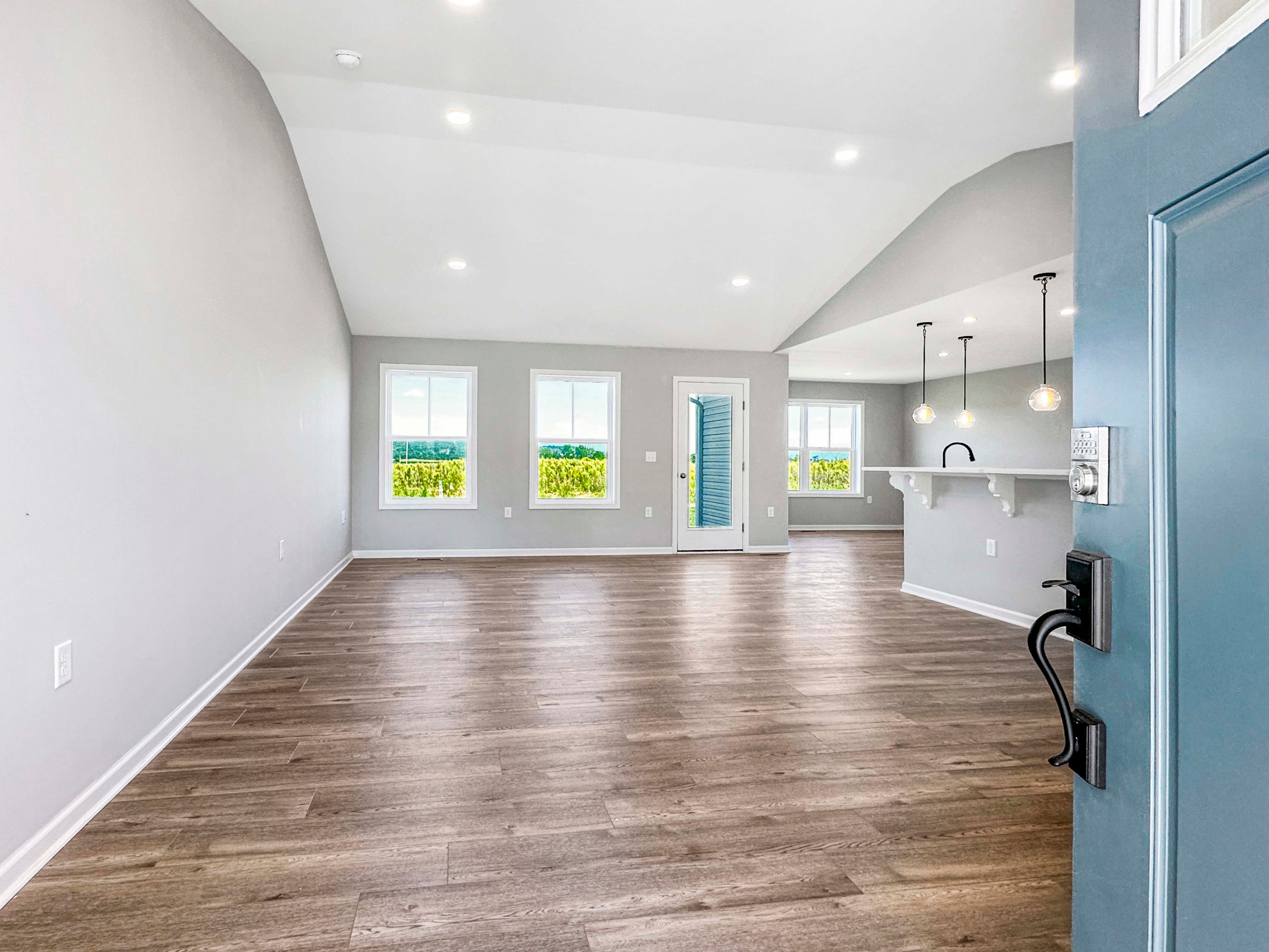 Unfurnished great room with vaulted ceiling, large windows, and wood-like flooring. Open floor plan with plenty of natural light.