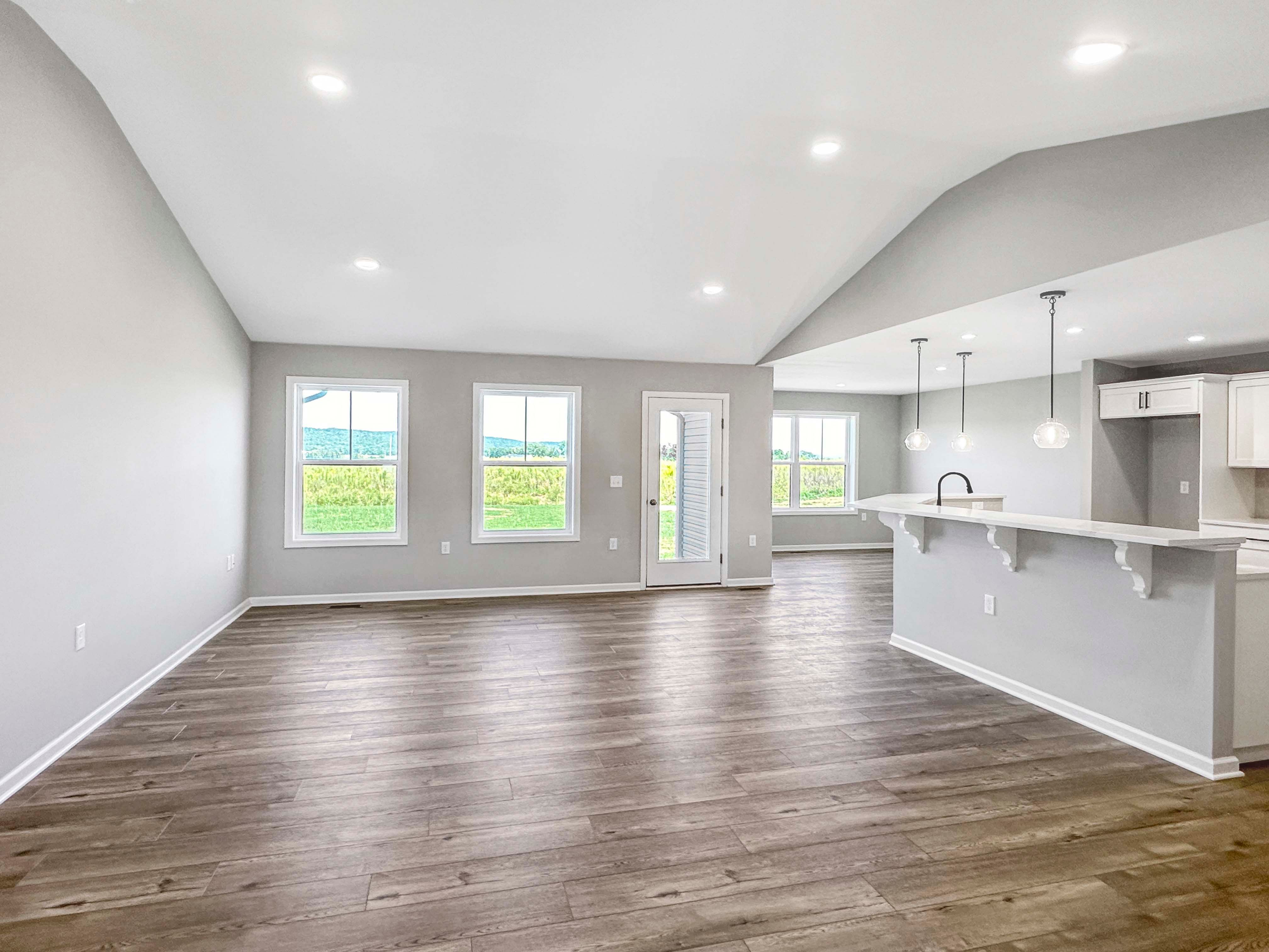 Bright and open great room with wood-like flooring and large windows, leading to an exterior door.