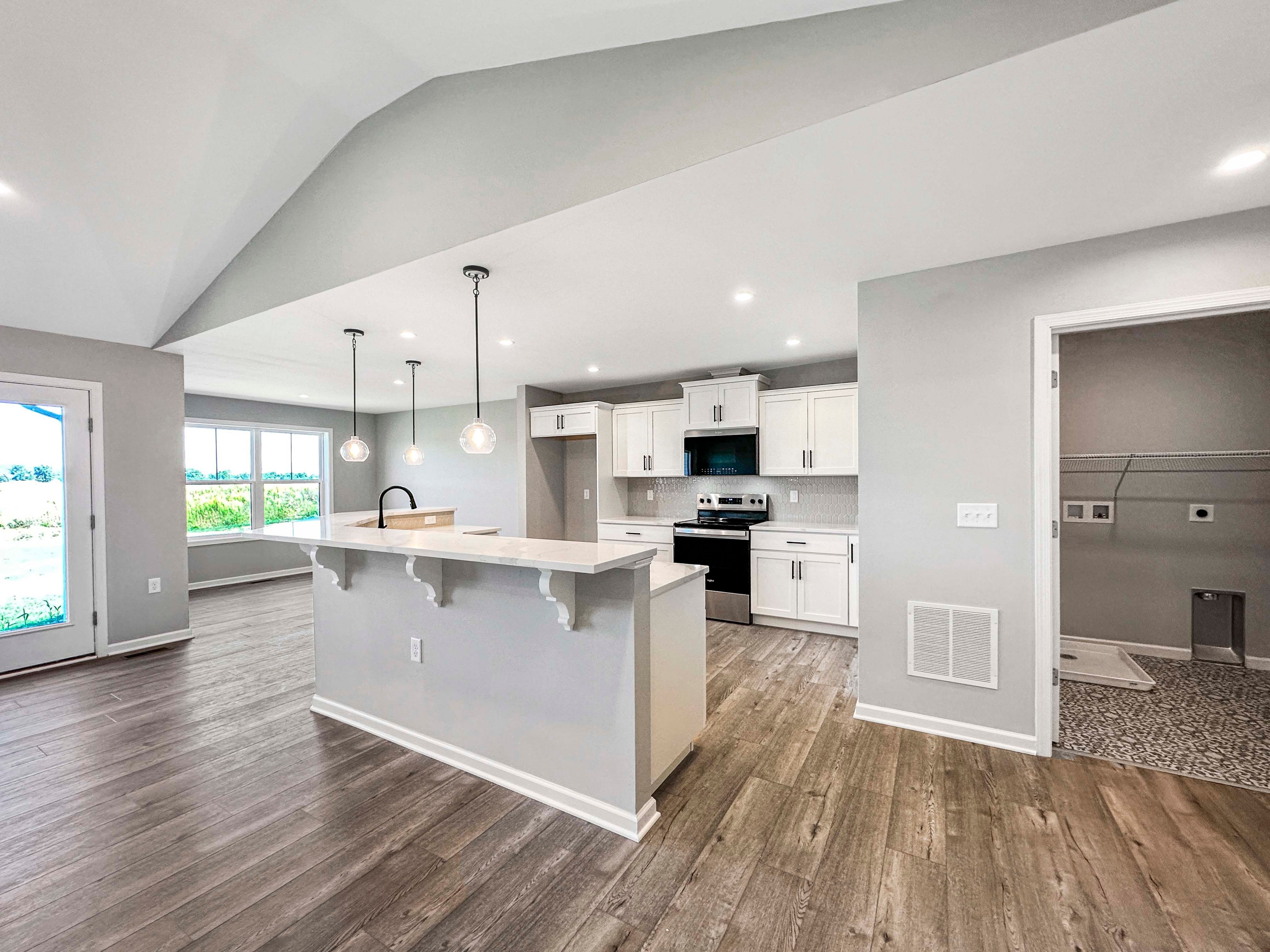 Modern kitchen with white cabinetry, stainless steel appliances, and pendant lighting. Open to the breakfast nook with large windows.