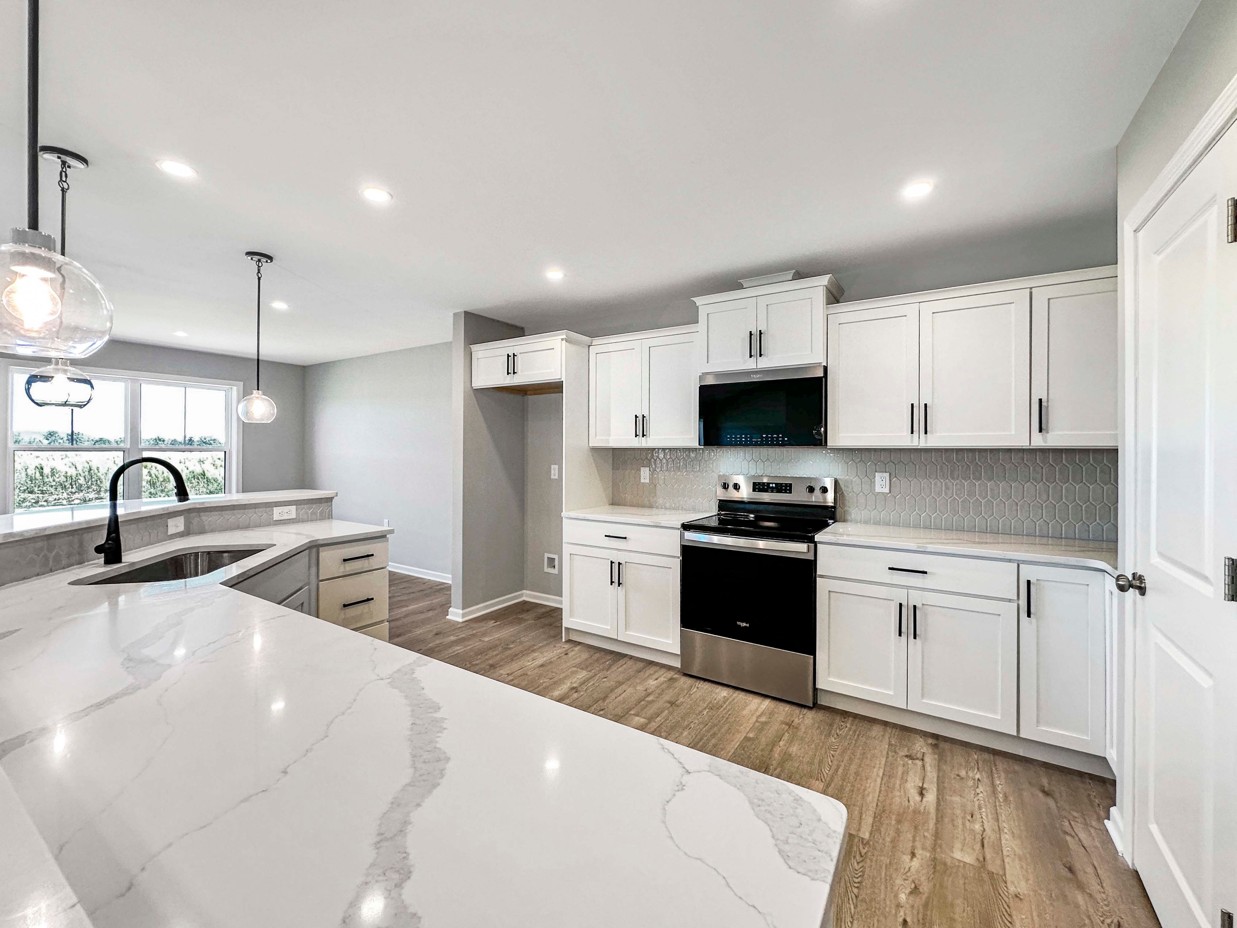 Bright kitchen featuring white quartz countertops, gray hexagonal tile backsplash, and sleek black appliances. Pendant lights hang above the island.