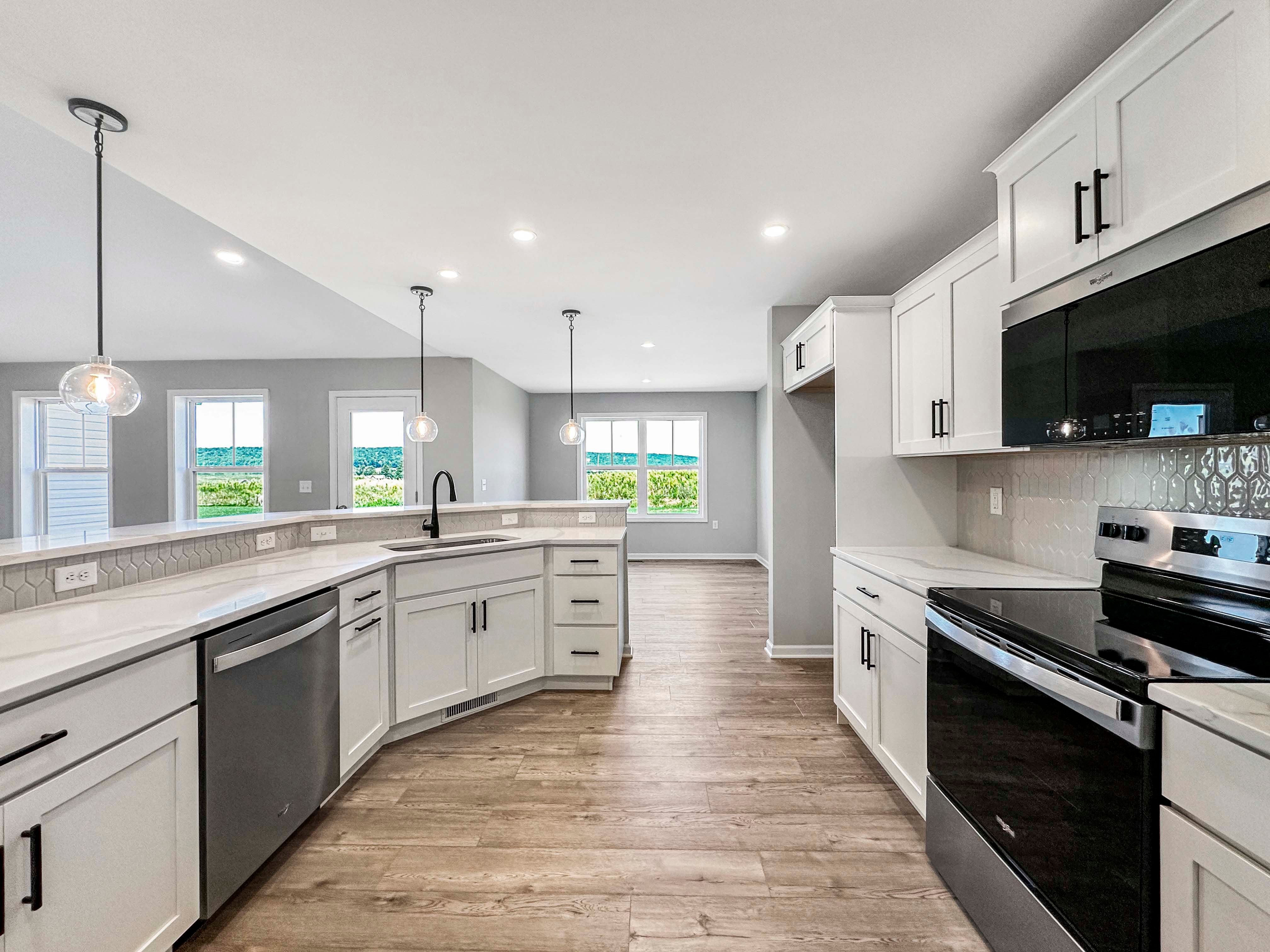 Spacious kitchen with a large island, white cabinetry, black hardware, and a built-in stainless steel oven. Pendant lights add elegance.