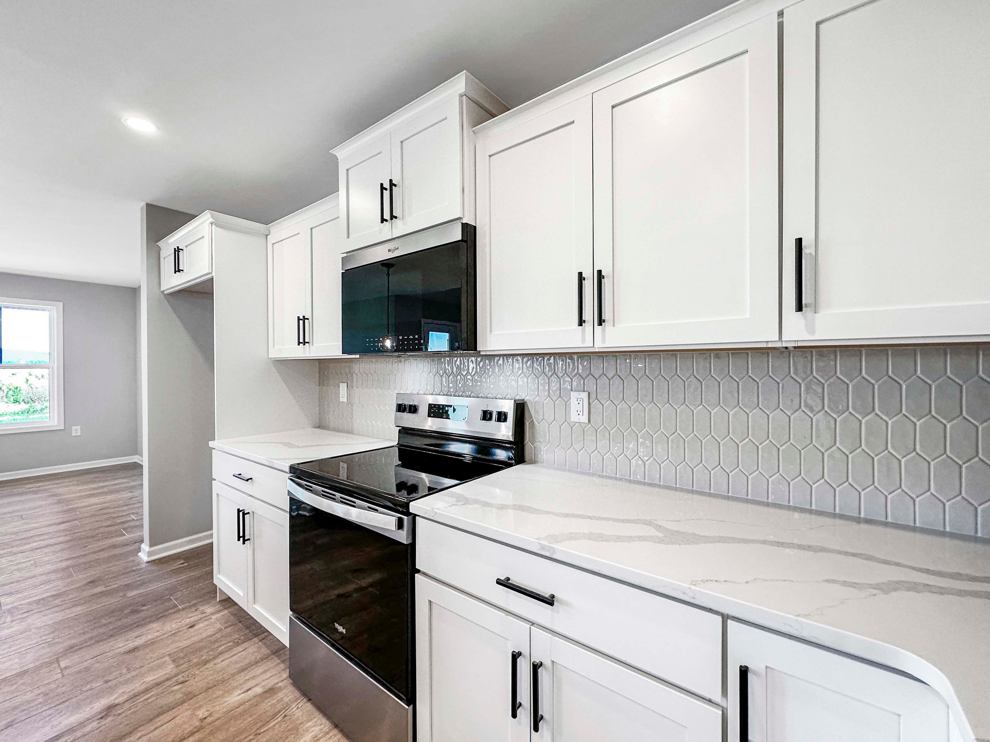 Open kitchen with a large island, stainless steel appliances, and hexagonal tile backsplash. Pendant lights illuminate the space.