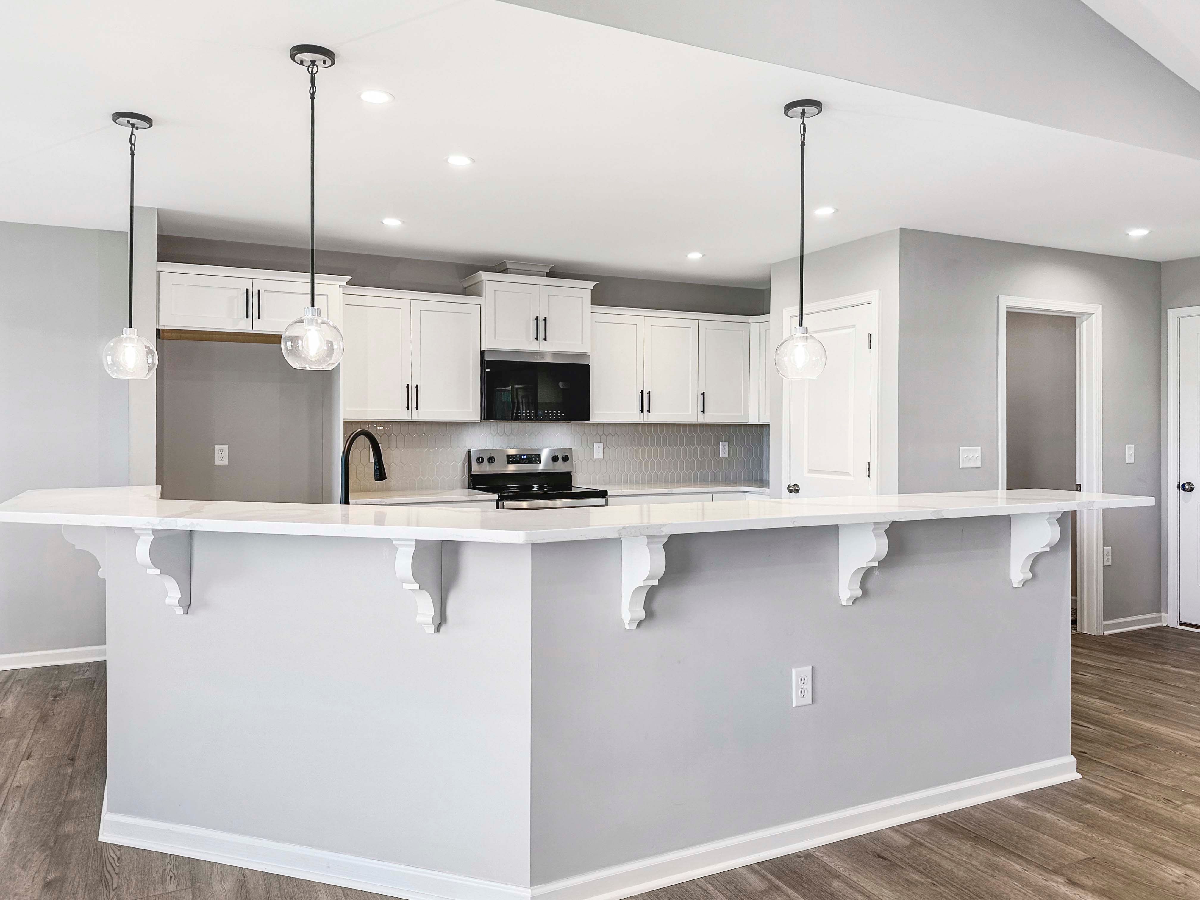 Spacious kitchen with pendant lighting, black fixtures, and white cabinetry. Stainless steel appliances and wood-like flooring throughout.