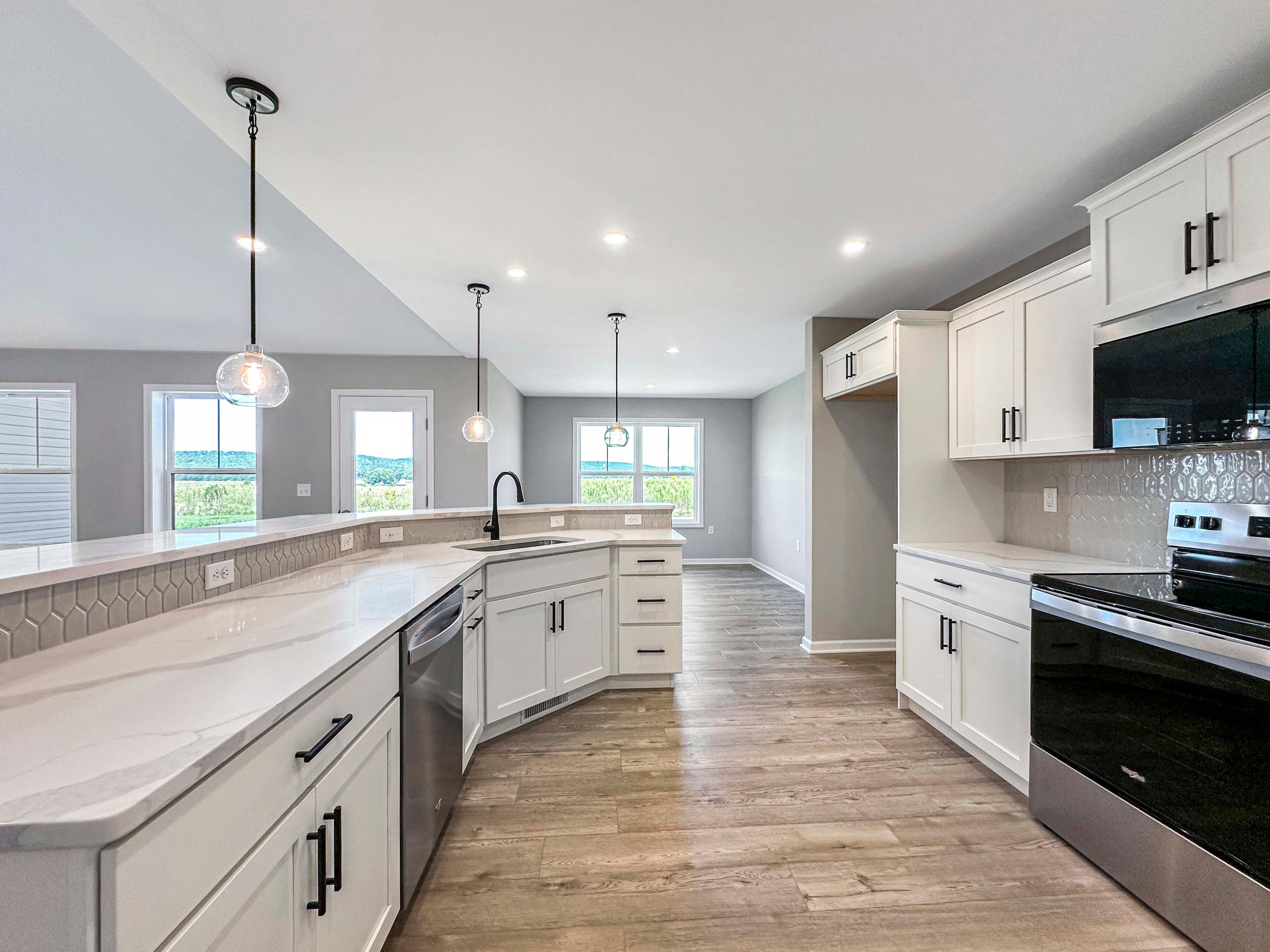 Bright kitchen with a large island, white cabinetry, and a stainless steel oven. Hexagonal tile backsplash and pendant lights.