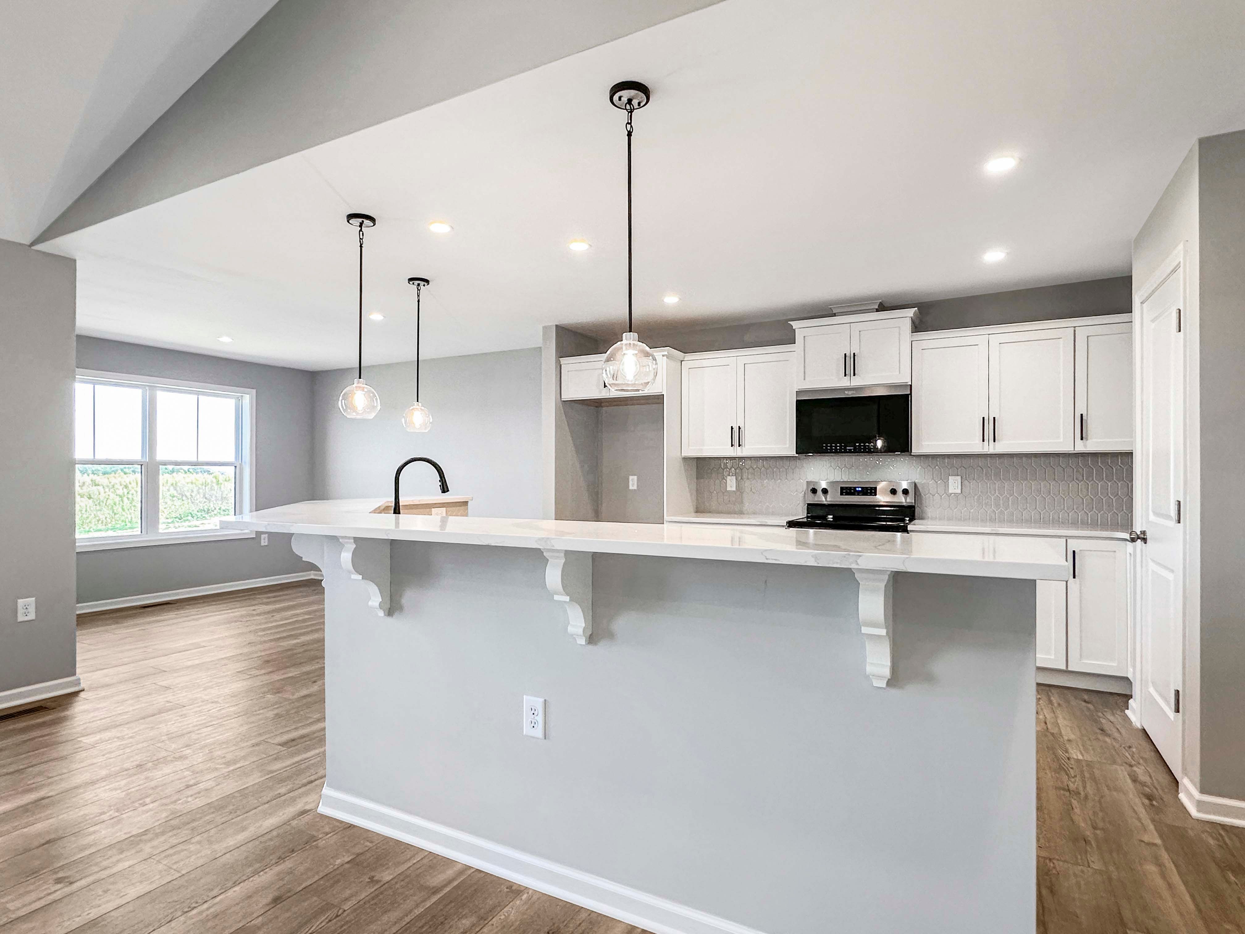 Open-concept kitchen with white cabinets, black hardware, and stainless steel appliances. Wood-like flooring extends through the kitchen.