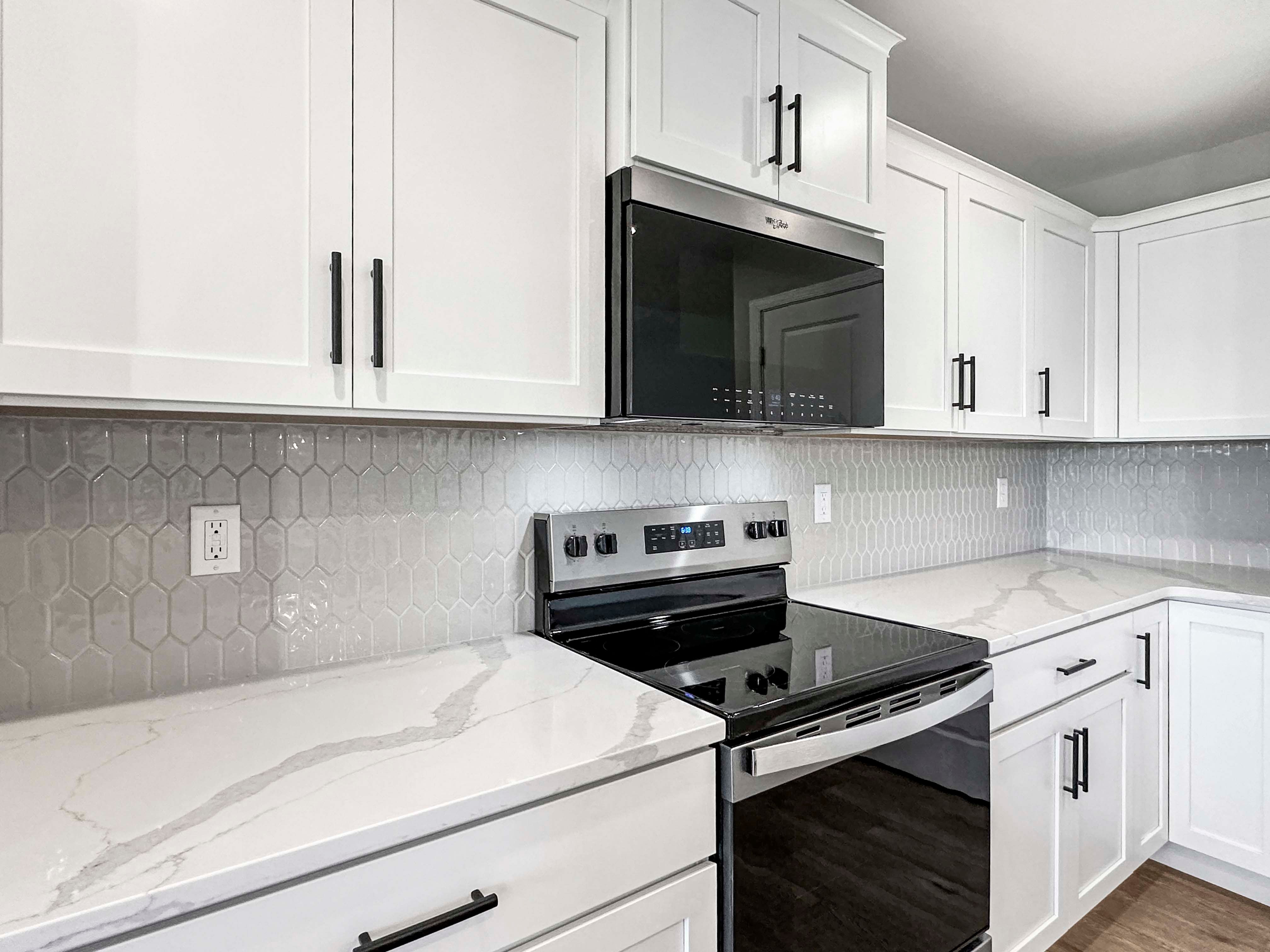 Bright kitchen with white shaker cabinets, marbled quartz countertops, black hardware, and a hexagon-patterned tile backsplash.